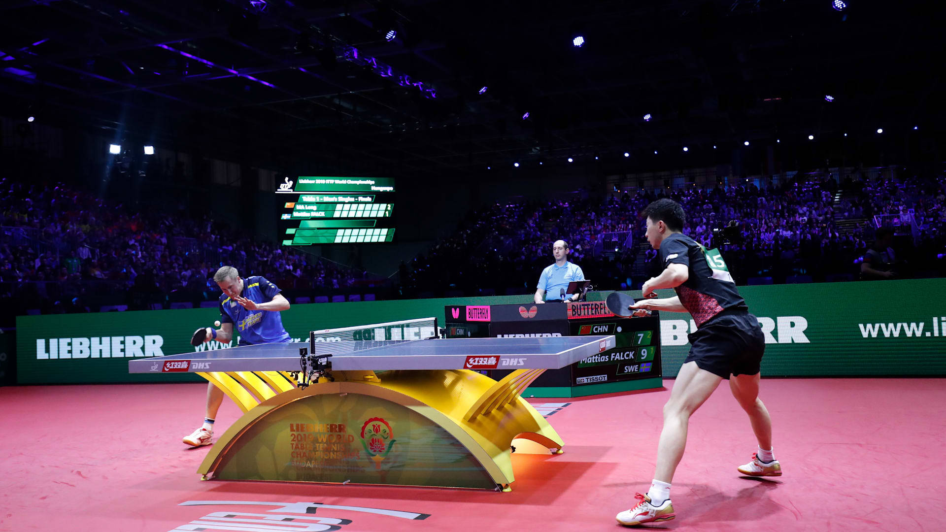 Table Tennis 桌布 壁紙 — 兩名乒乓球運動員在紫色燈光下，於光線明亮的場館內與擠滿的人群激烈競爭。