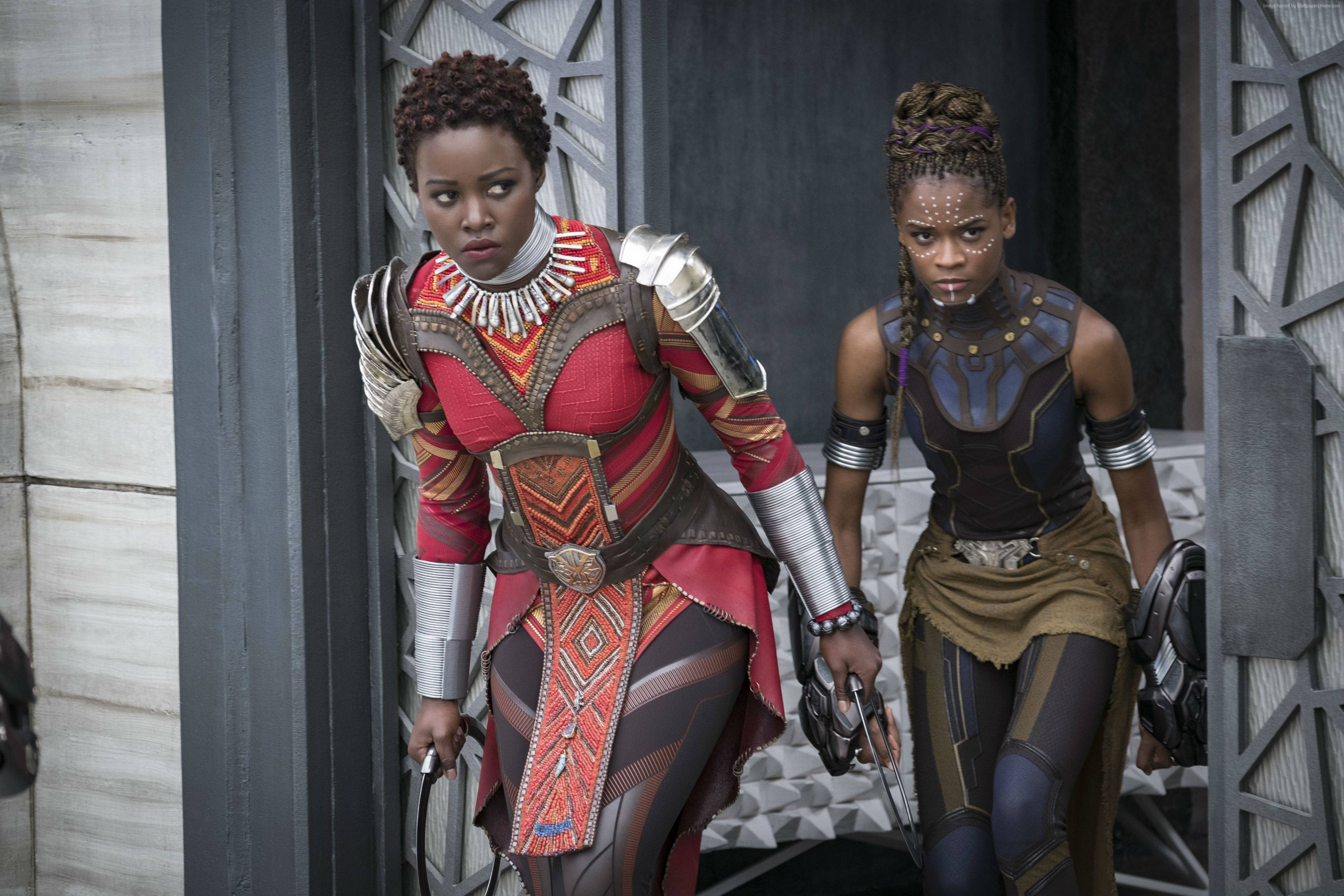 Shuri 桌布 壁紙 — 兩名兇猛的女戰士身穿精細的紅色和藍色盔甲，在未來主義的門口警覺地站著。