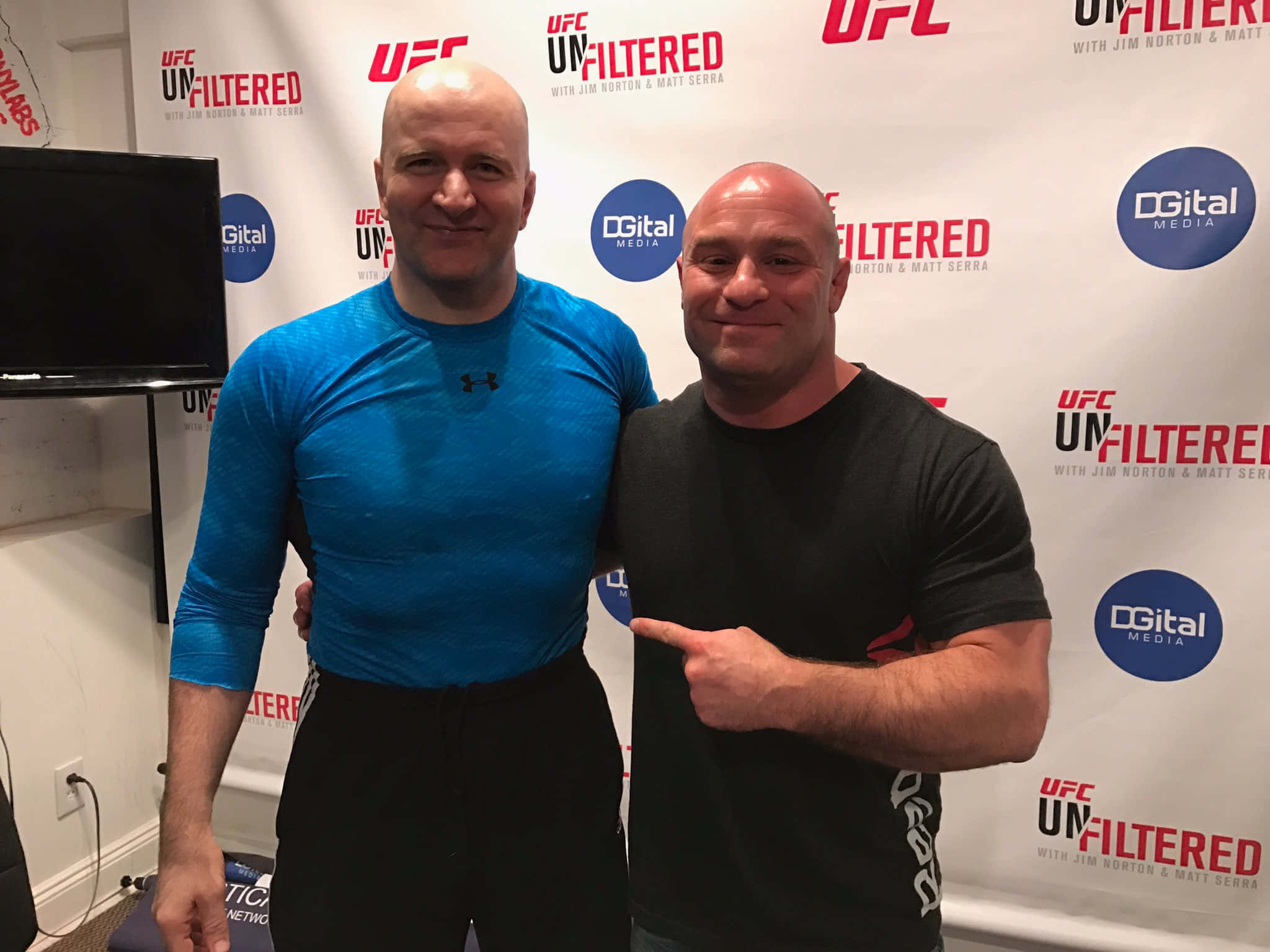 UFC 桌布 壁紙 — 兩名光頭男子穿著運動服，在UFC品牌背景前微笑擺姿勢，其中一人指向另一人。