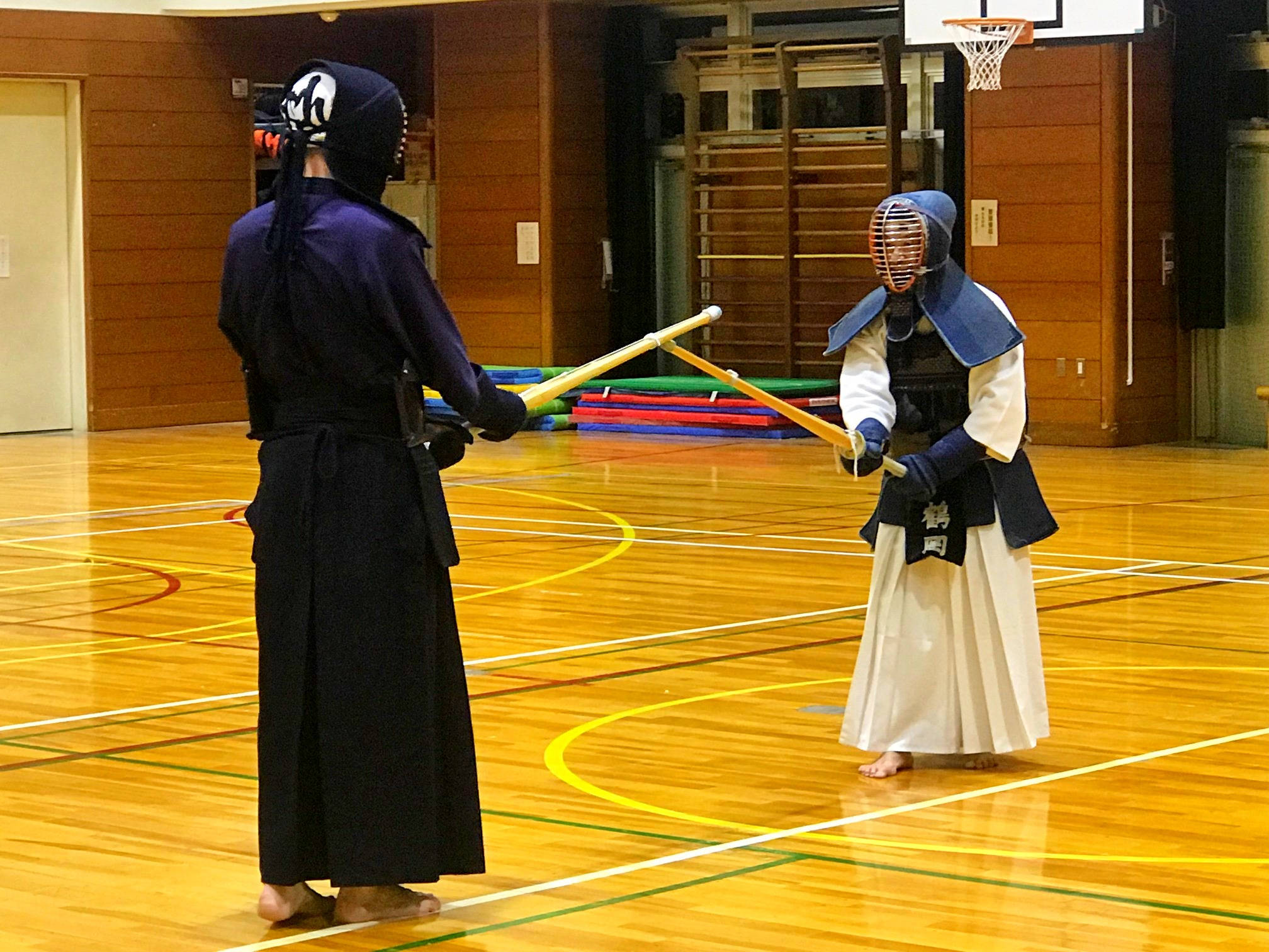 運動 桌布 壁紙 — 兩名全副裝備的劍道練習者在明亮的室內燈光下，於拋光木質體育館地板上交劍。