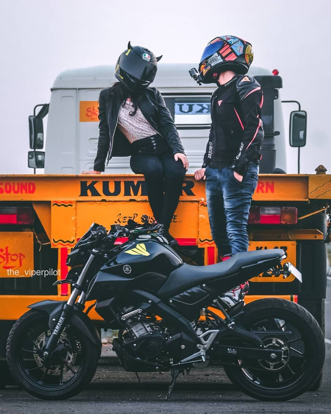 Couple 桌布 壁紙 — 兩名全副裝備的摩托車手在一輛亮橙色卡車上擺姿勢，前面停著一輛時尚的黑色摩托車。