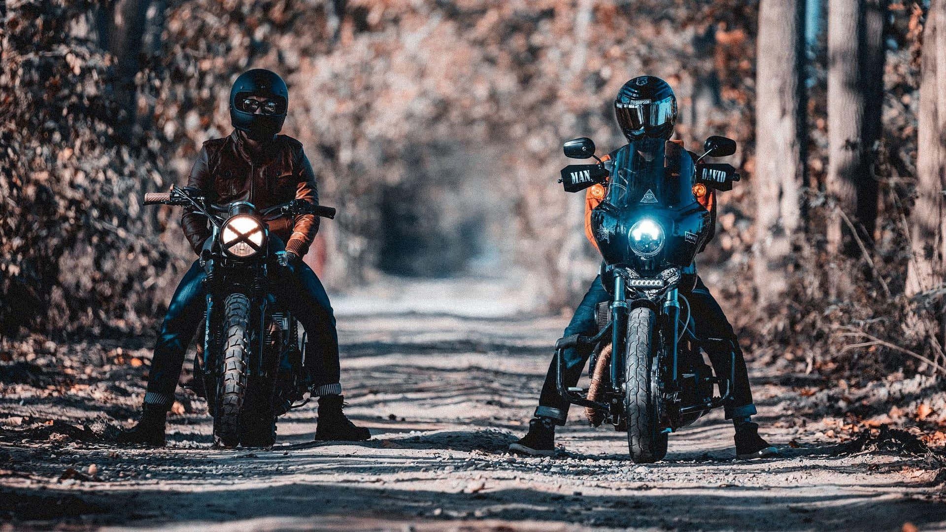 biker 桌布 壁紙 — 兩名全副裝備的摩托車手在鋪滿落葉的森林道路上停下來，車頭燈亮著。