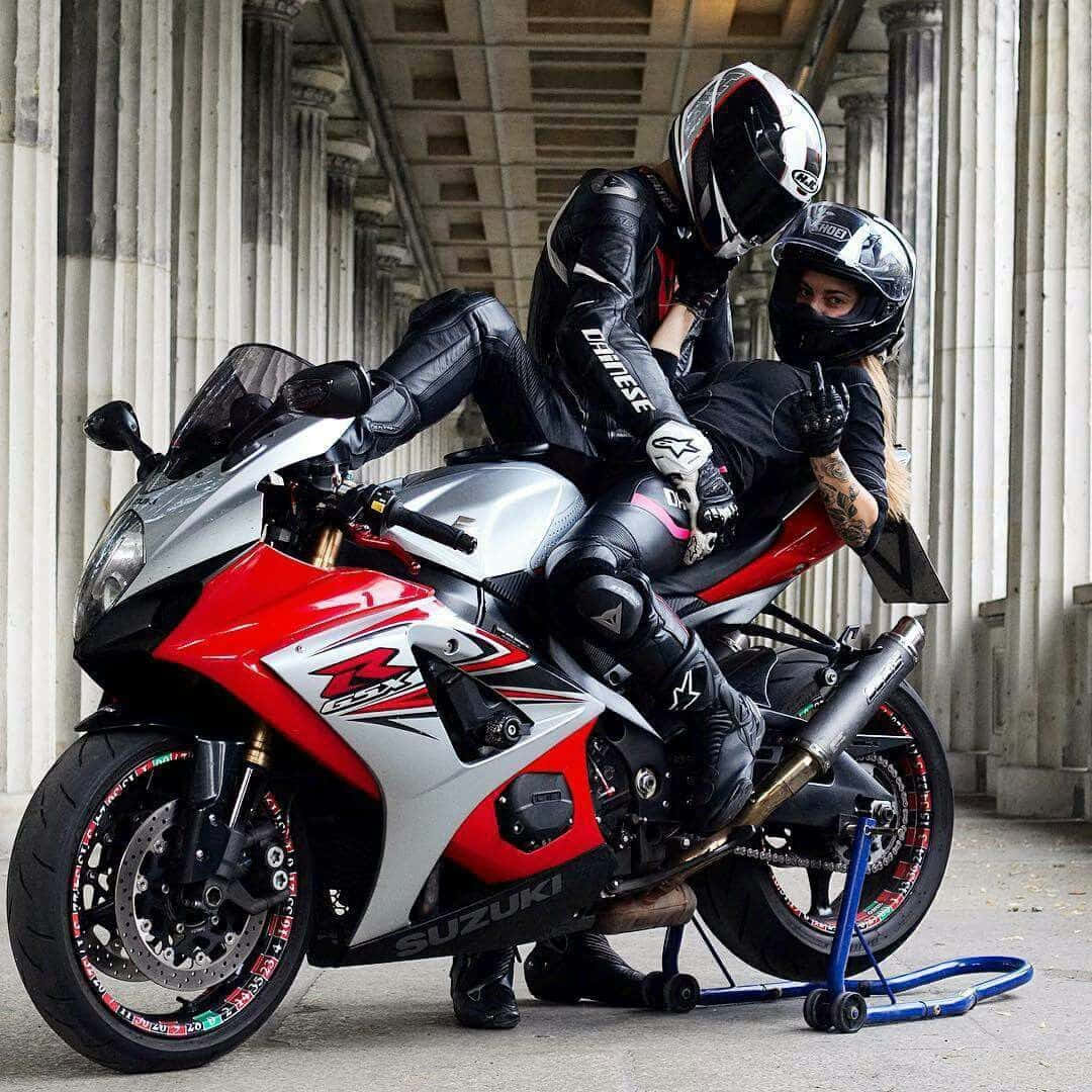 Lovers 桌布 壁紙 — 兩名全副裝備的機車騎士在經典石柱下，於一輛紅銀色鈴木跑車上親密擺姿勢。