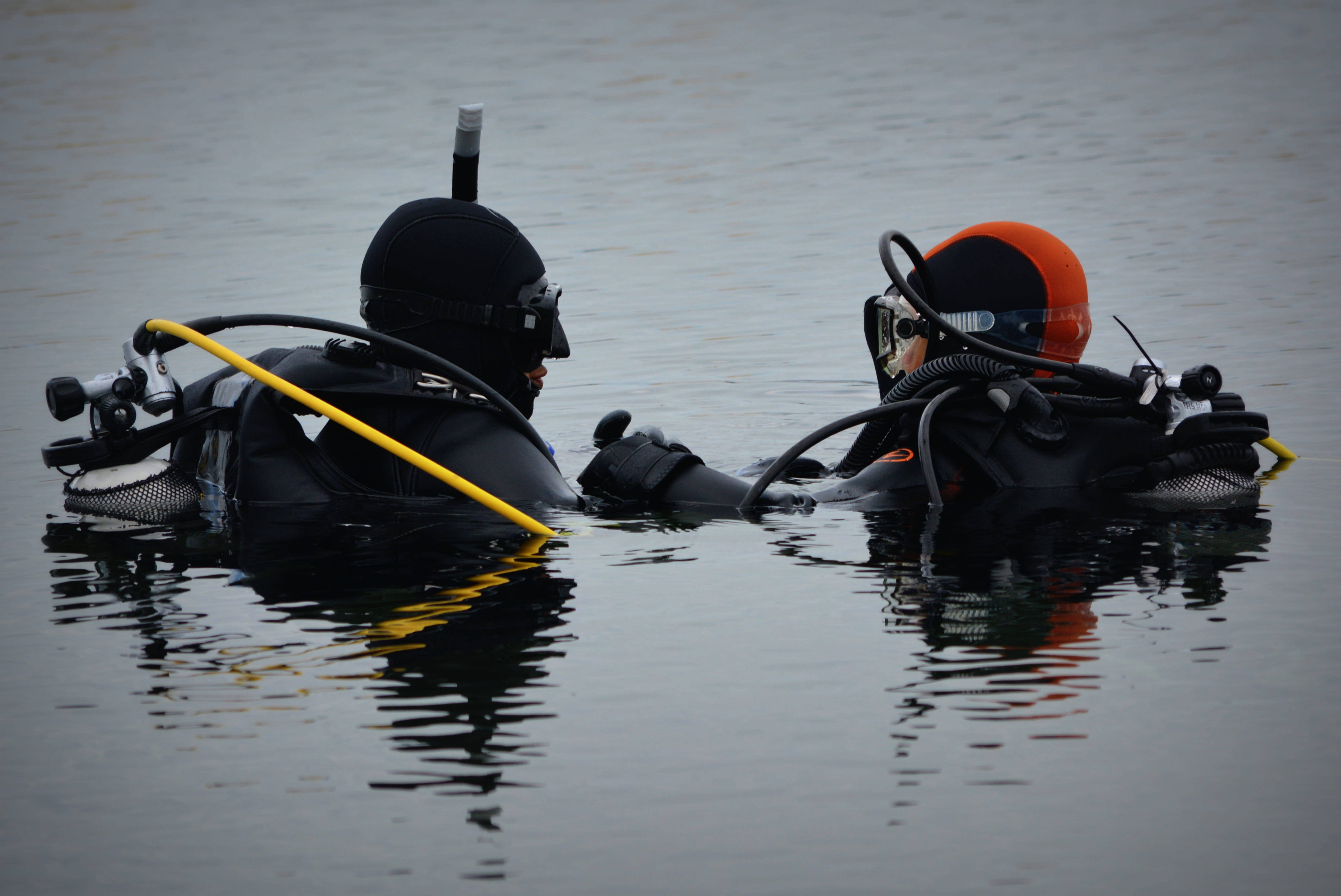 diving 桌布 壁紙 — 兩名全副裝備的水肺潛水員平靜地漂浮在平靜的水面上，交換手勢。