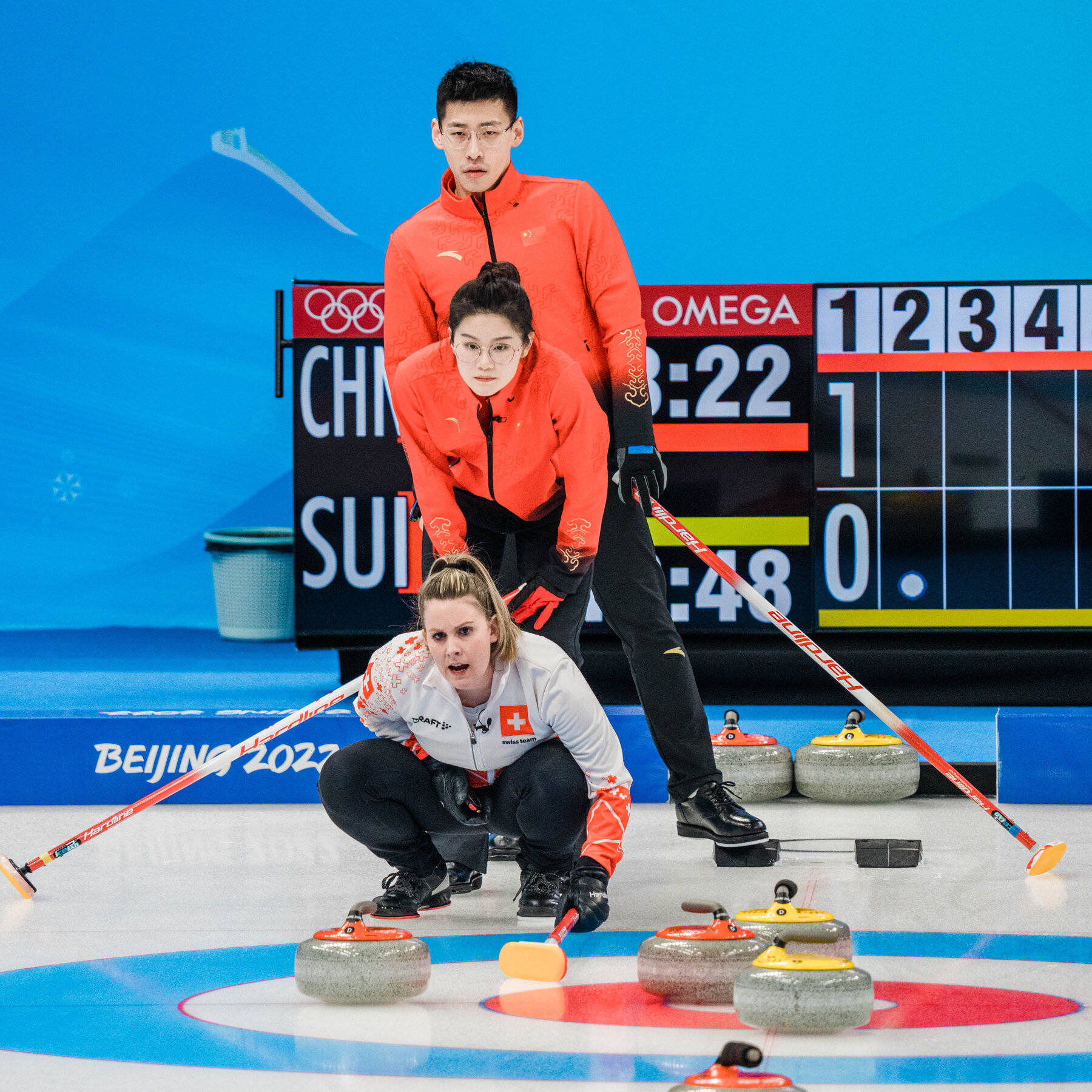 Olympics 桌布 壁紙 — 兩名冰壺運動員在冰場上專注比賽，場內有記分牌和冰壺石。