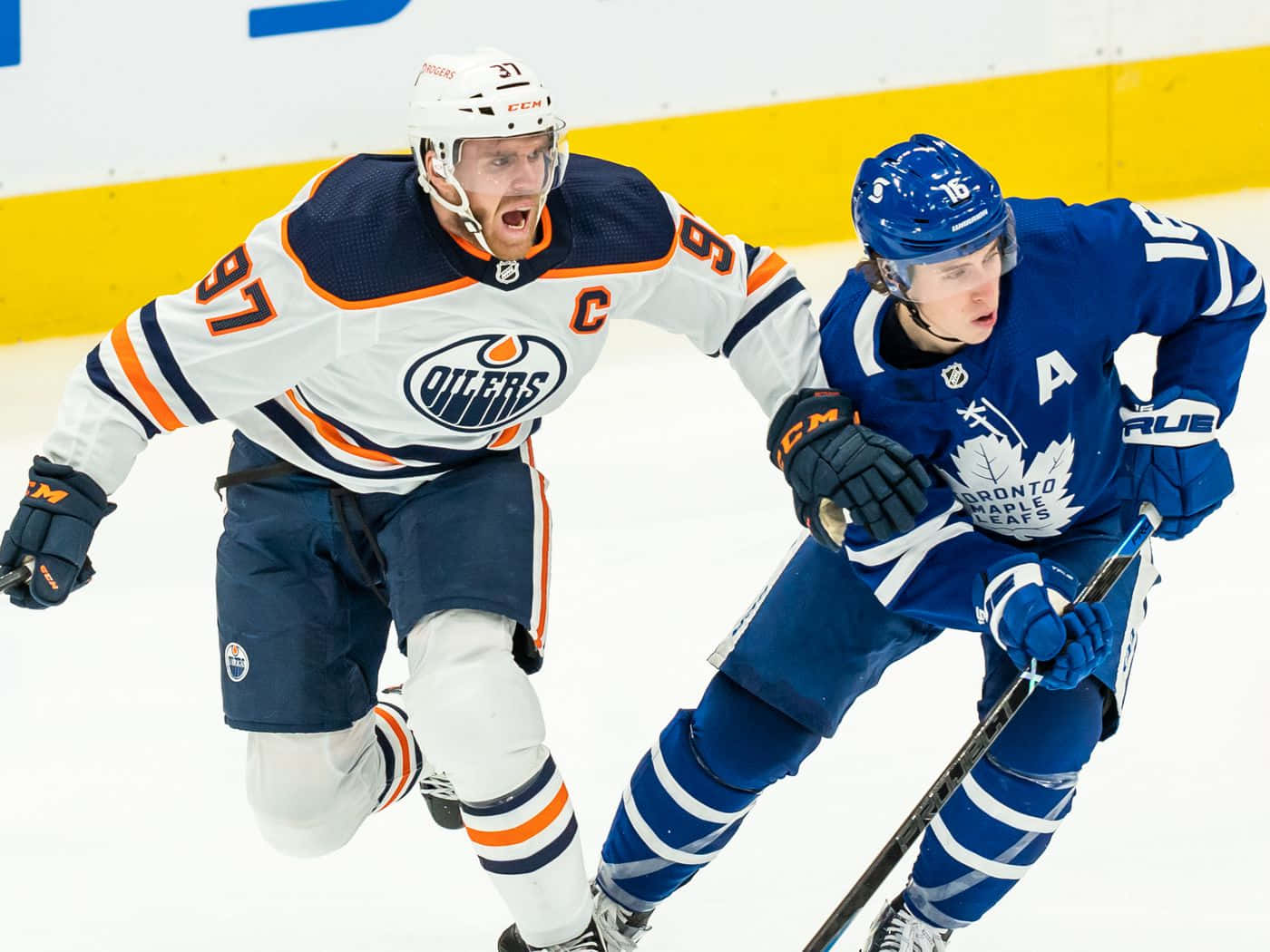 Connor Mcdavid 桌布 壁紙 — 兩名冰球運動員在冰上比賽，一人身穿白色Oilers球衣，帶有隊長C標誌，另一人身穿藍色Leafs球衣，兩人在比賽中高度專注。