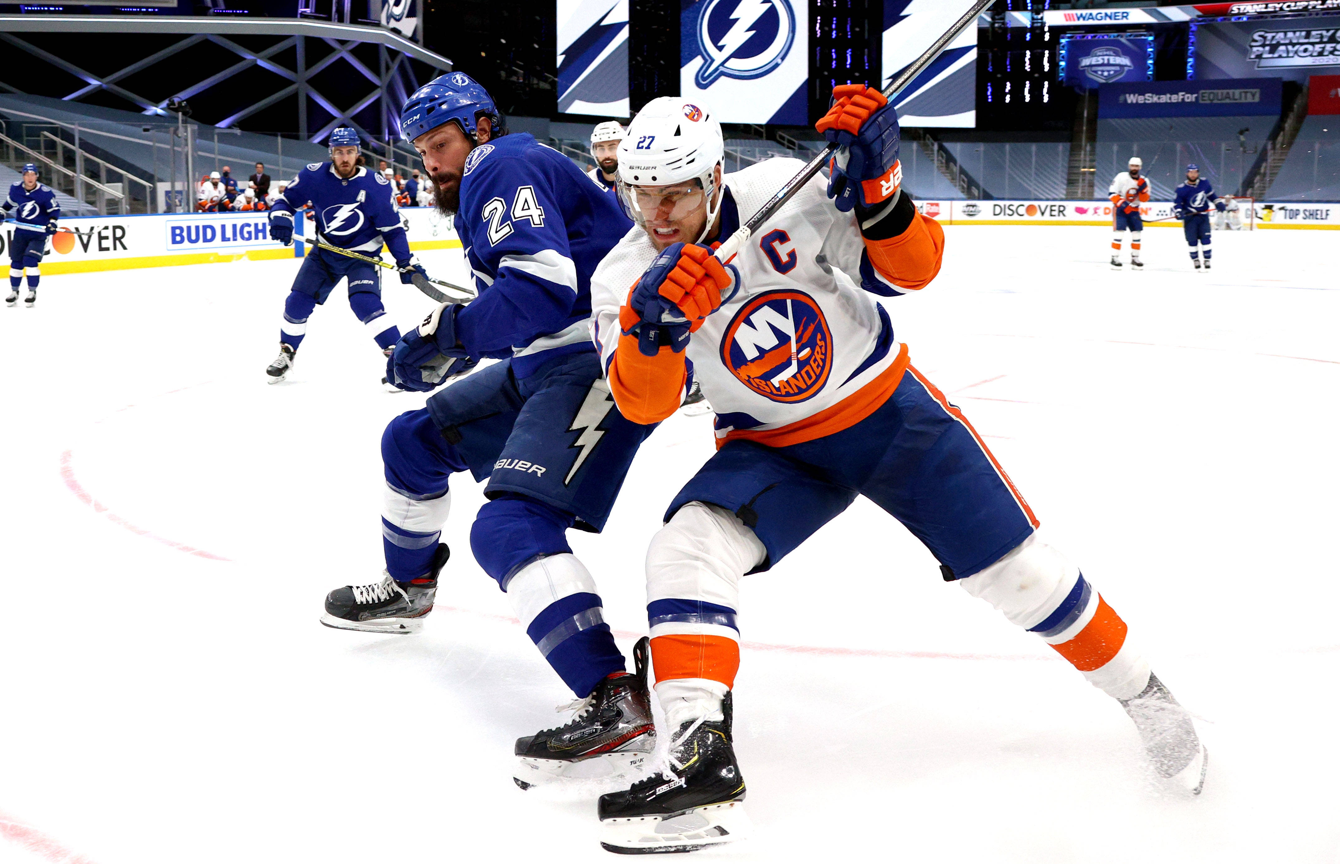 New York Islanders 桌布 壁紙 — 兩名冰球運動員在冰上激烈對抗，一人身穿白橙色制服並帶有隊長C標誌，另一人身穿藍色制服，兩人都專注且堅定。