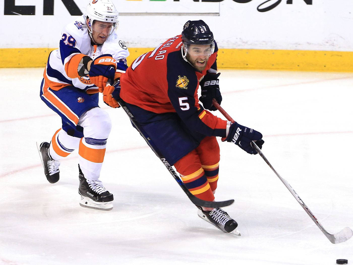 hockey 桌布 壁紙 — 兩名冰球運動員在冰上激烈對抗，一人身穿紅藍色球衣，號碼5，另一人身穿白藍橙色球衣，號碼29。