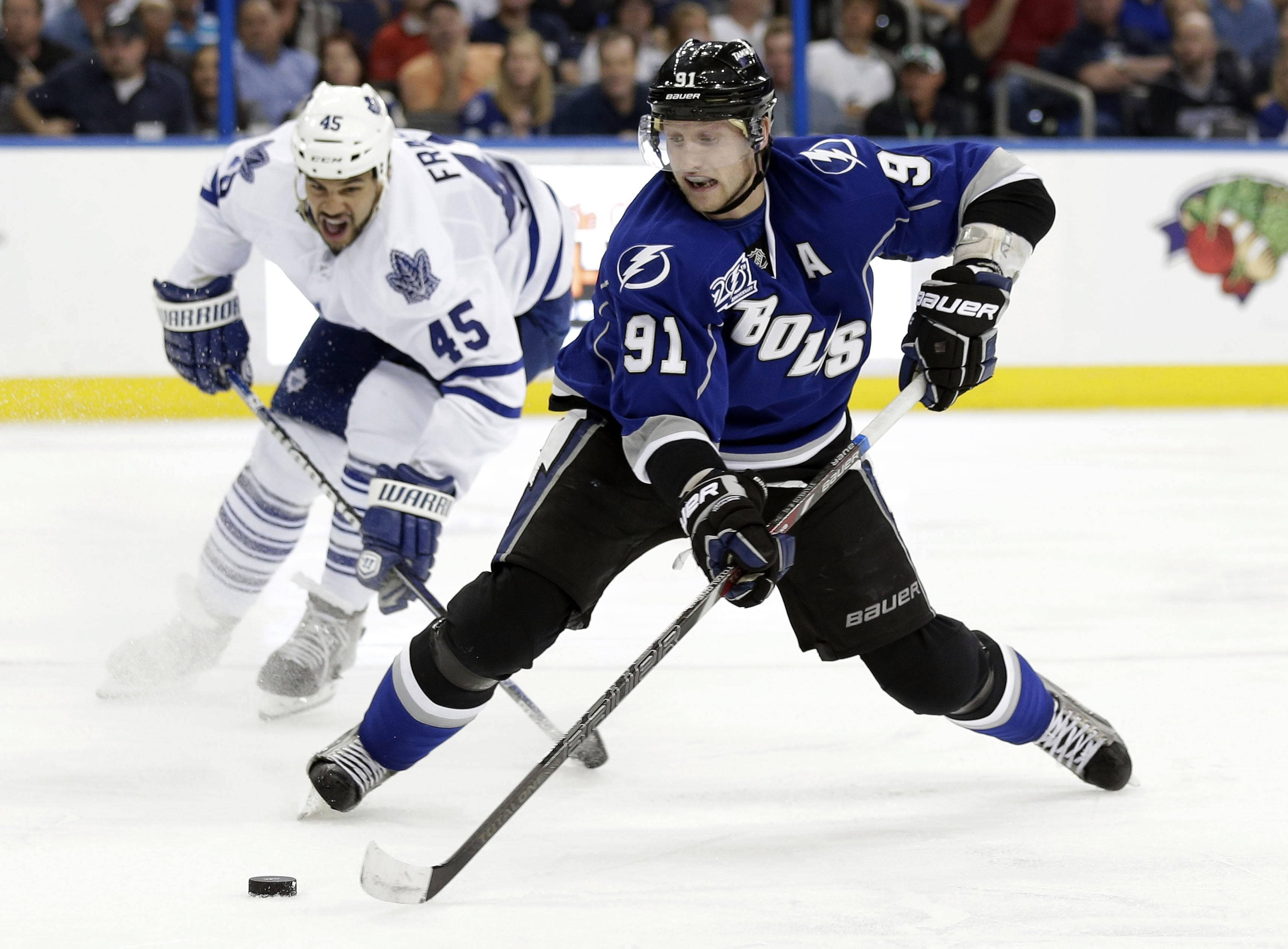 Tampa Bay Lightning 桌布 壁紙 — 兩名冰球運動員在冰上激烈爭奪，藍色球衣的球員控制著冰球，而白色球衣的對手向前猛撲。