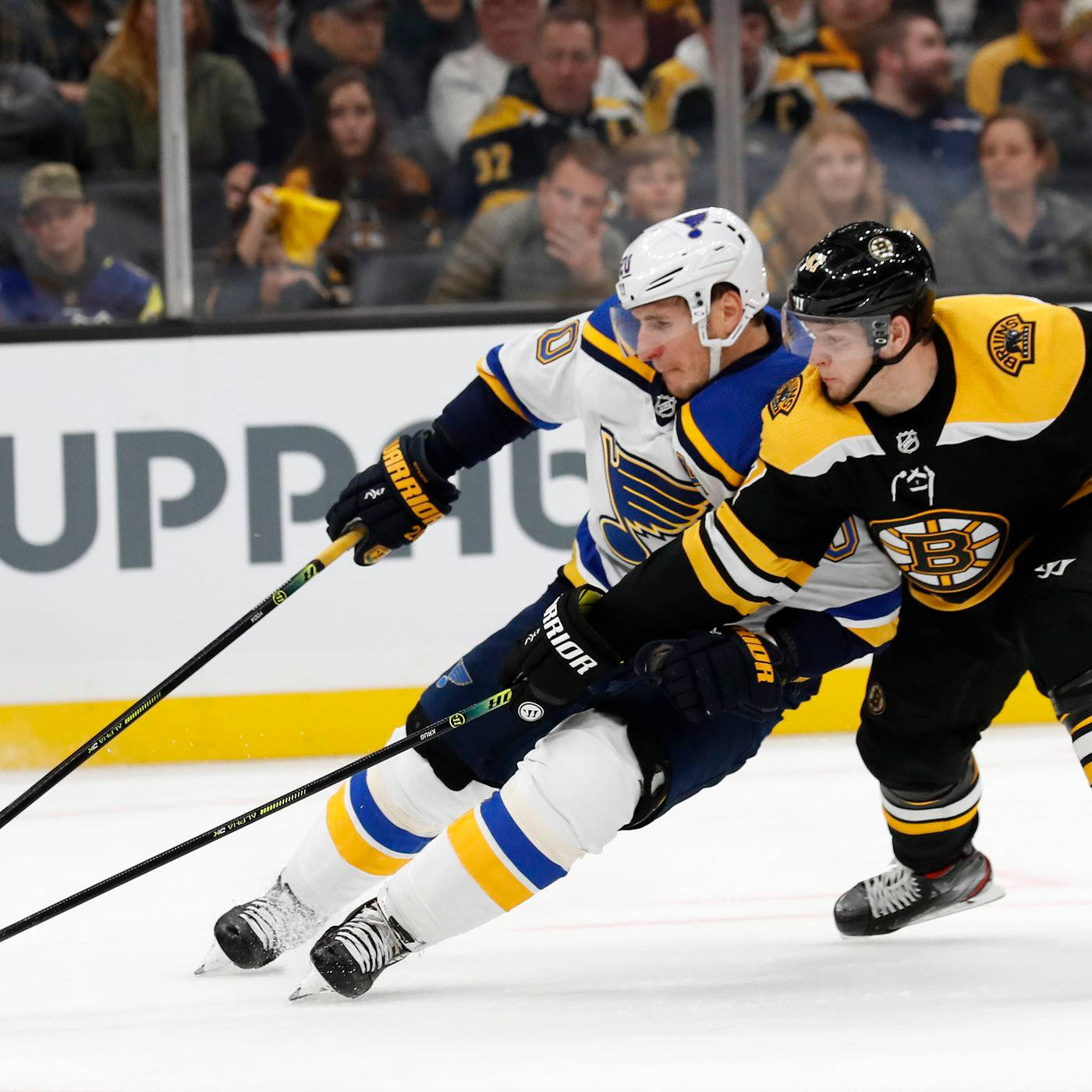 St Louis Blues 桌布 壁紙 — 兩名冰球運動員在冰上激烈爭奪控球權，觀眾在玻璃後面觀看。