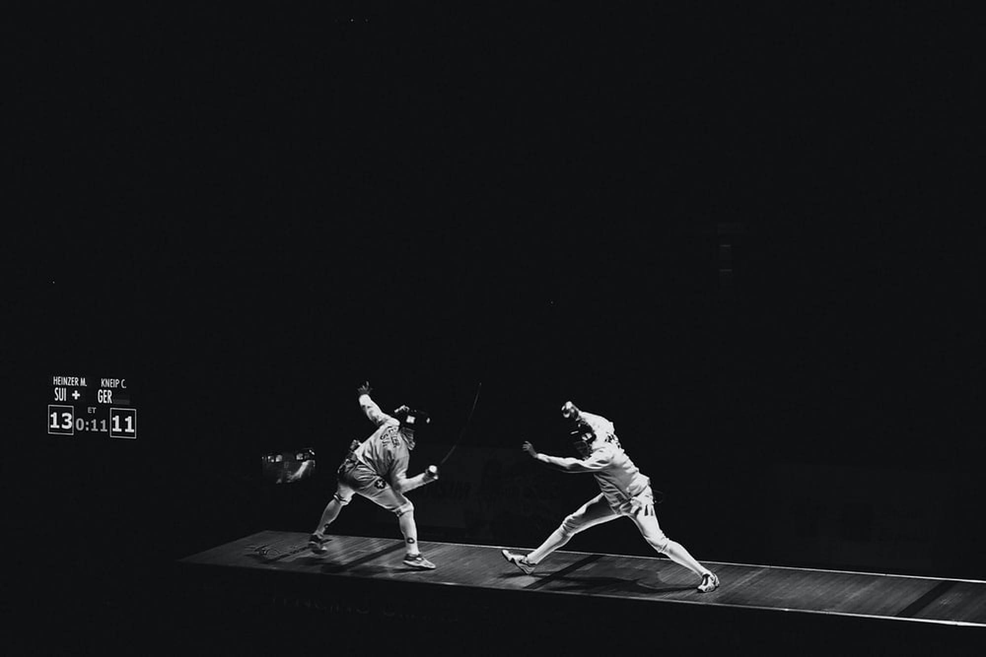 Fencing 桌布 壁紙 — 兩名劍擊運動員在昏暗舞台上戲劇性聚光燈下擺出動態戰鬥姿勢，計分板可見。