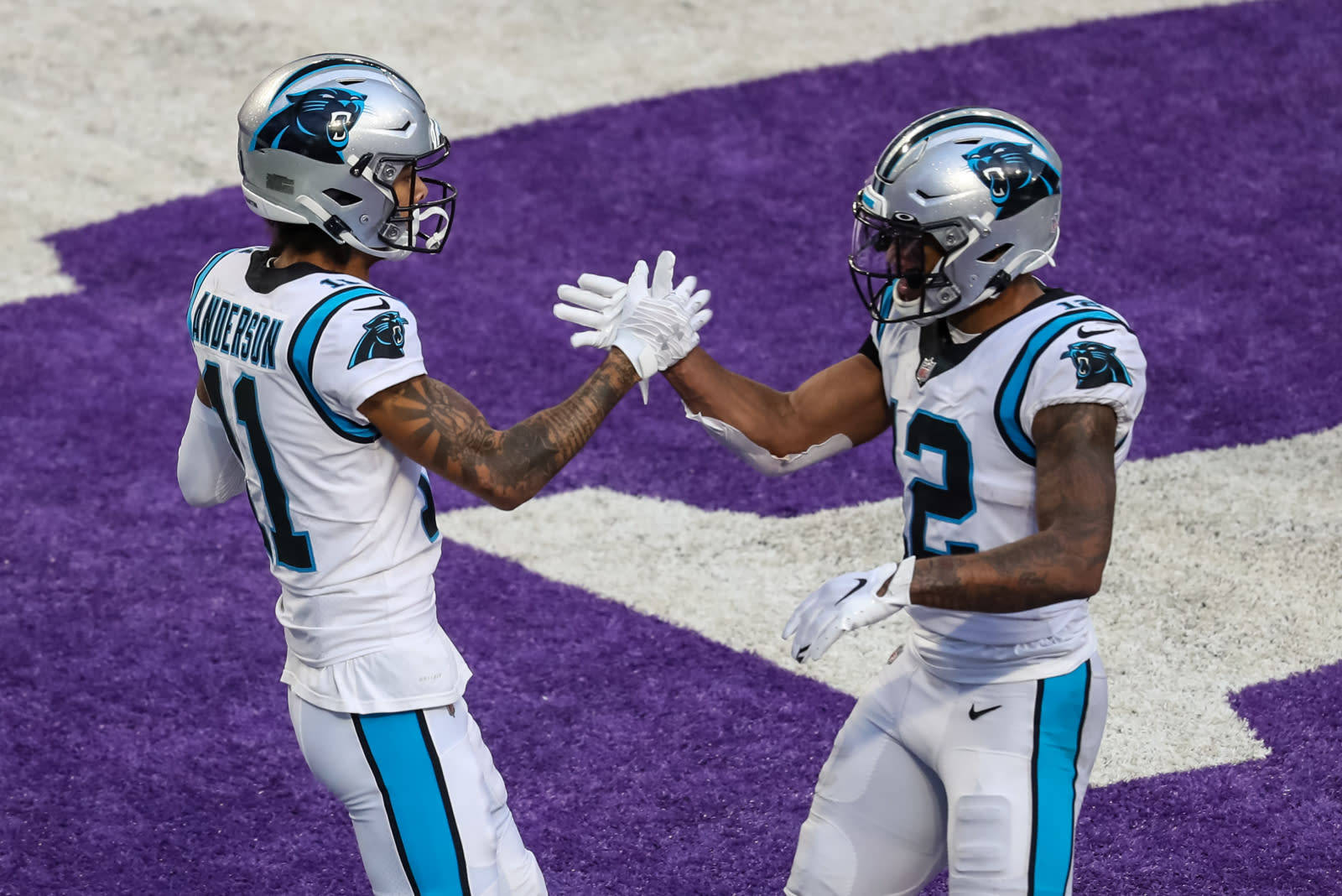 Panthers 桌布 壁紙 — 兩名卡羅萊納黑豹隊美式足球員身穿白色和青綠色球衣，在充滿活力的紫色和白色場地上擊掌。
