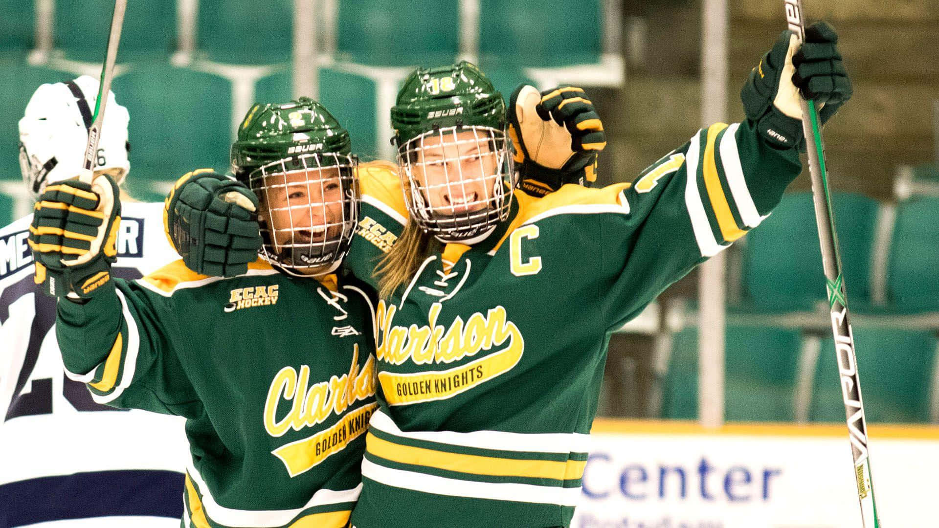 hockey 桌布 壁紙 — 兩名喜悅的Clarkson Golden Knights曲棍球球員在室內溜冰場高舉手臂和球棍慶祝進球。