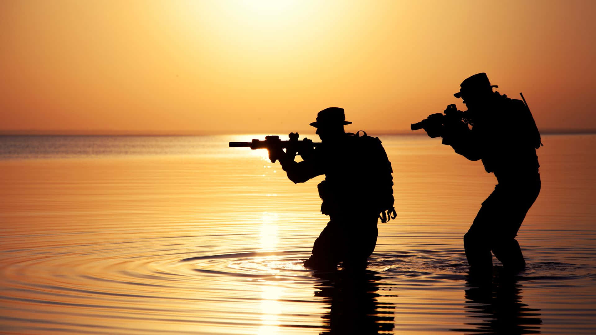 軍事動圖 桌布 壁紙 — 兩名士兵在剪影中涉水而過，手持步槍，夕陽在他們身後落下，灑下金色光芒。