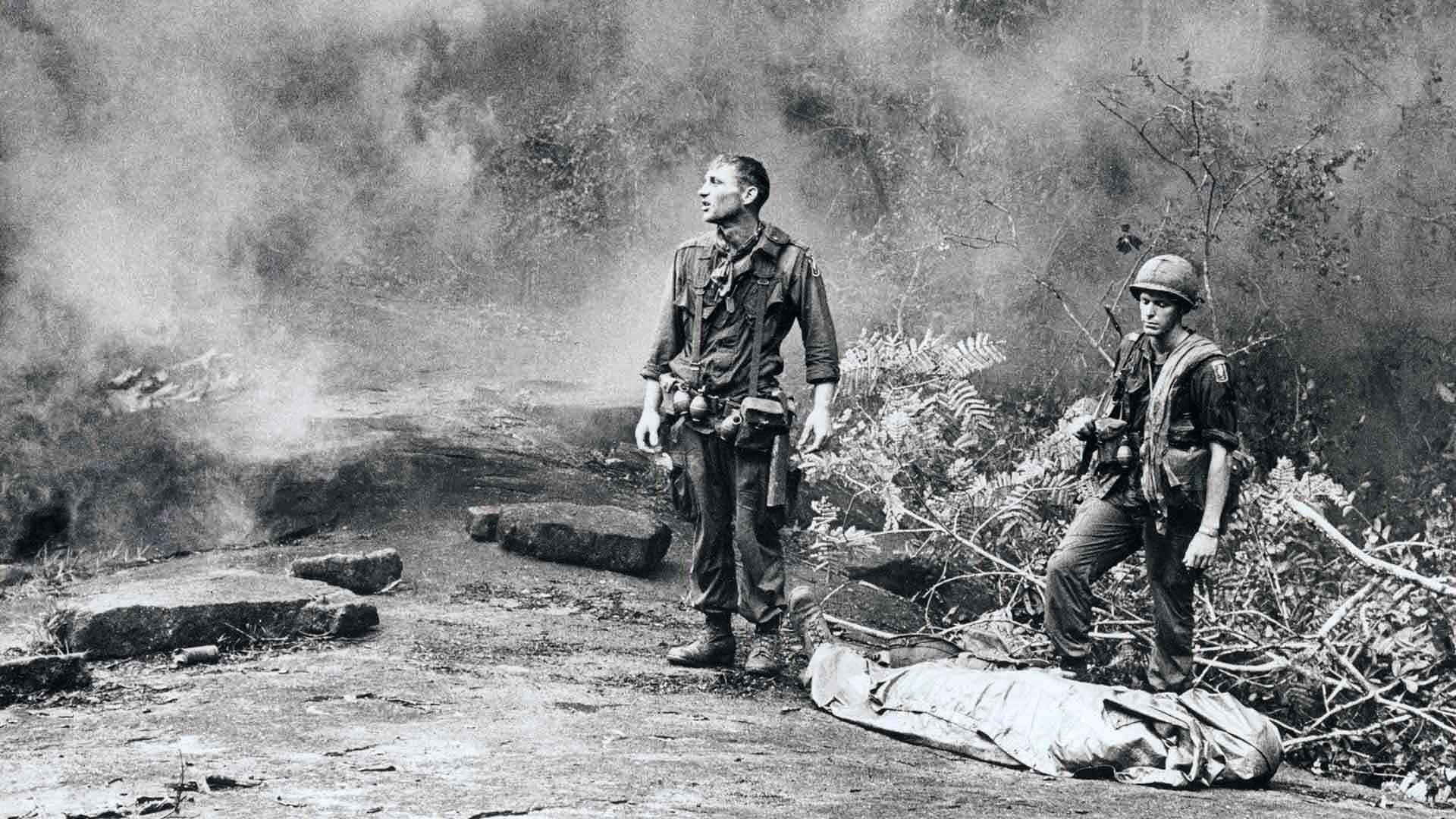越南 桌布 壁紙 — 兩名士兵在叢林地形中，站在煙霧和碎片中用防水布包裹的屍體旁邊。