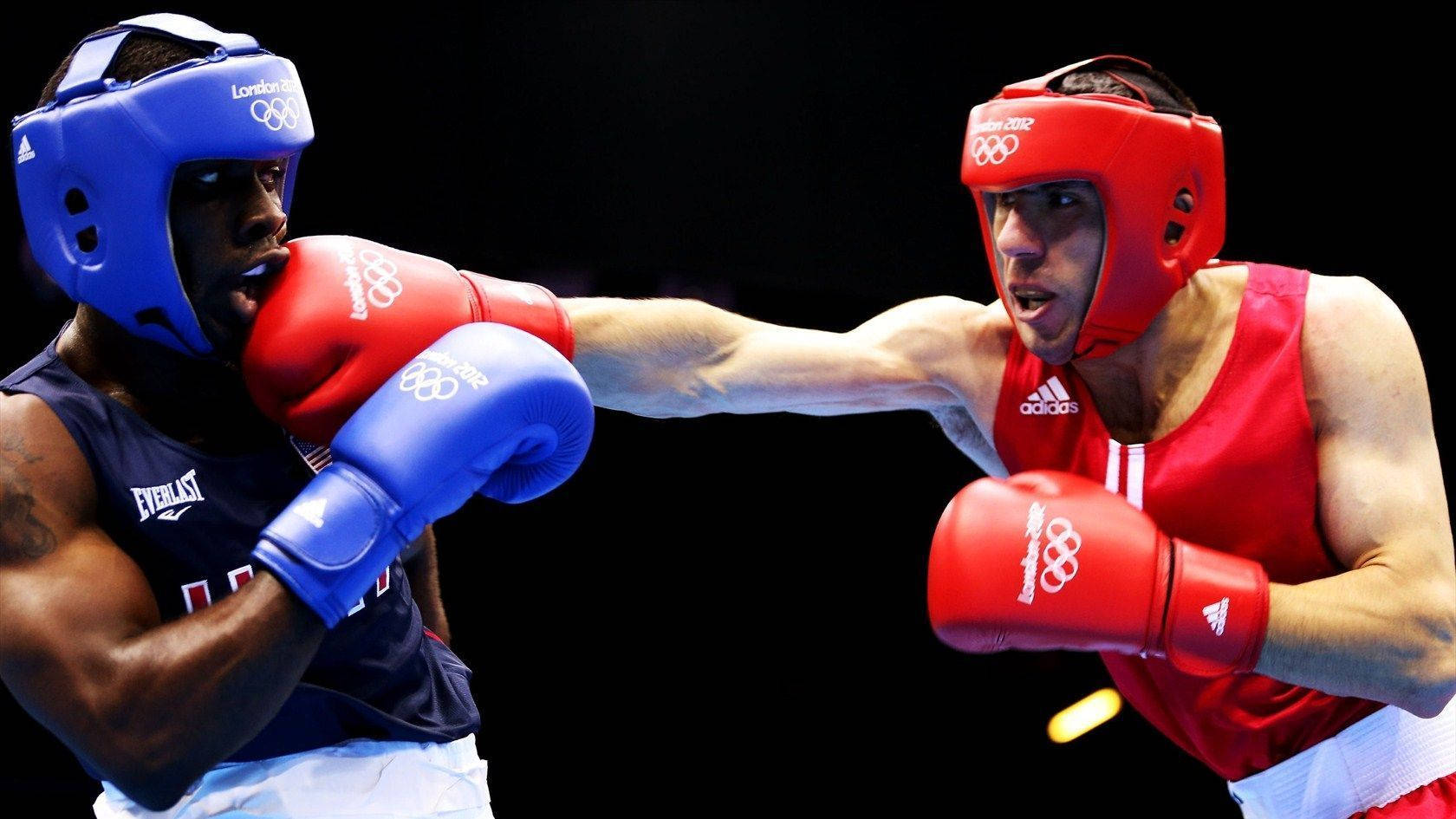 Boxing 桌布 壁紙 — 兩名奧運拳擊手身穿紅色和藍色裝備，在明亮的場館燈光下，於黑色背景前進行拳擊碰撞。