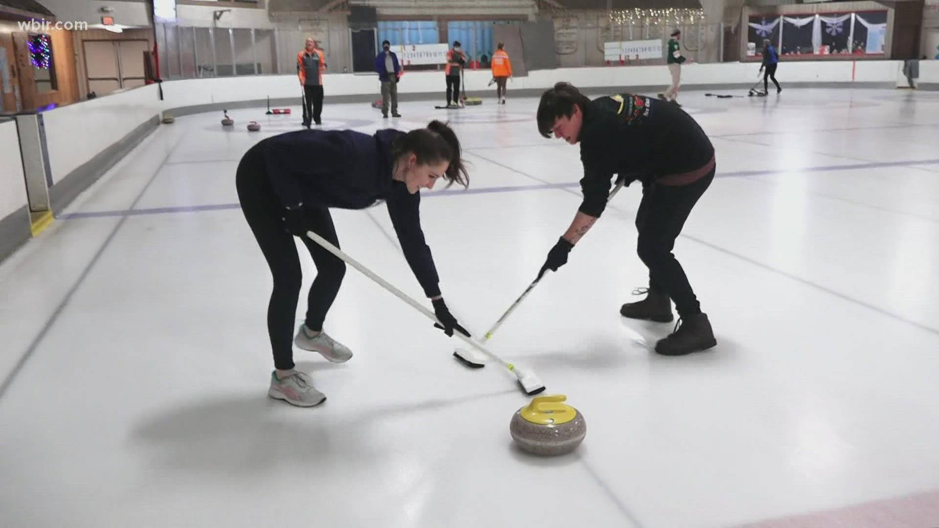 Olympics 桌布 壁紙 — 兩名女子在室內溜冰場用掃帚掃冰，冰壺向前滑行，背景有其他選手。