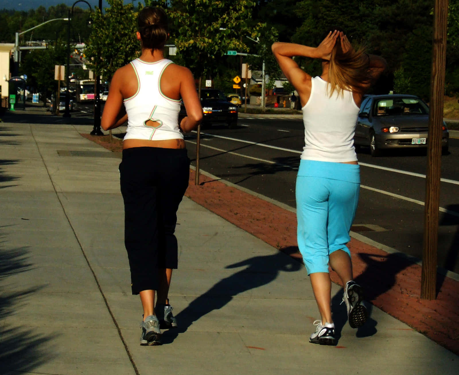Fitness 桌布 壁紙 — 兩名女子在陽光明媚的城市人行道上慢跑，車輛駛過時投下長長的影子。