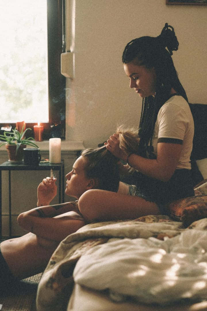 女同志 桌布 壁紙 — 兩名女子在陽光明媚的臥室中，一人為另一人編辮子，同時手持香煙。