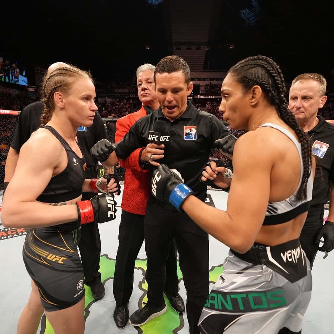 UFC 桌布 壁紙 — 兩名女性MMA拳手在明亮的場館燈光下，於UFC八角籠中對峙，裁判在中間。