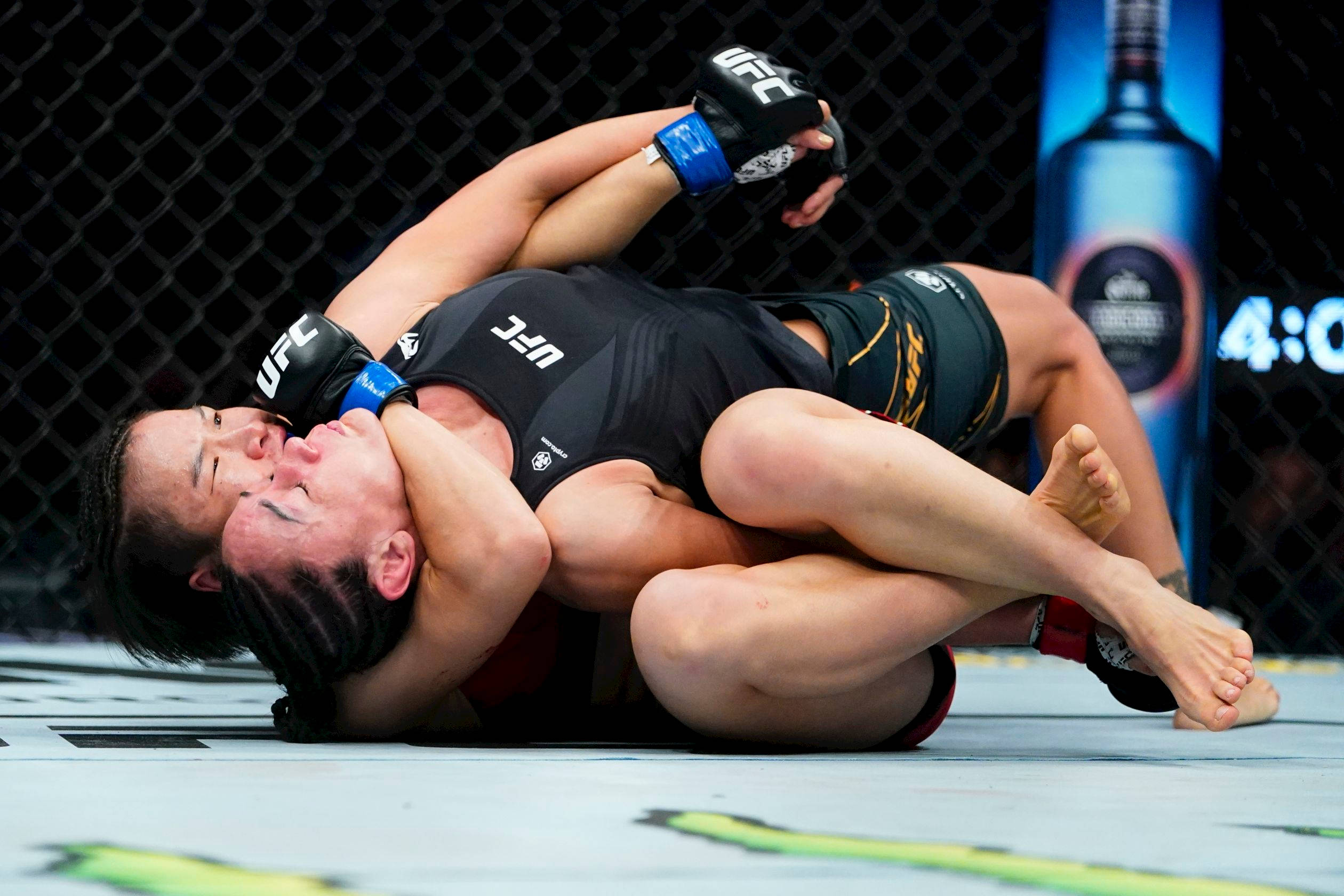 Athletic 桌布 壁紙 — 兩名女性MMA拳手在明亮的場館燈光下，於UFC比賽期間在籠內地板上激烈纏鬥。