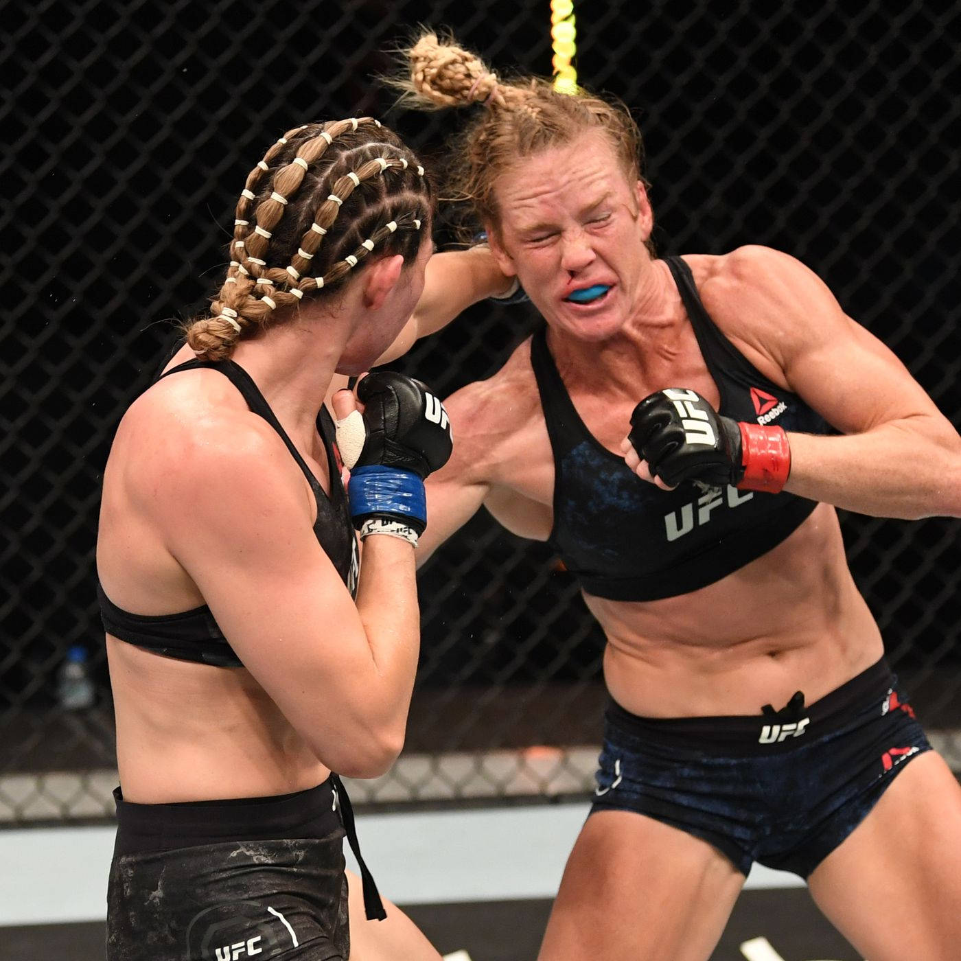 MMA 桌布 壁紙 — 兩名女性MMA拳手在激烈的籠中比賽中交鋒，汗水飛濺，表情兇猛。