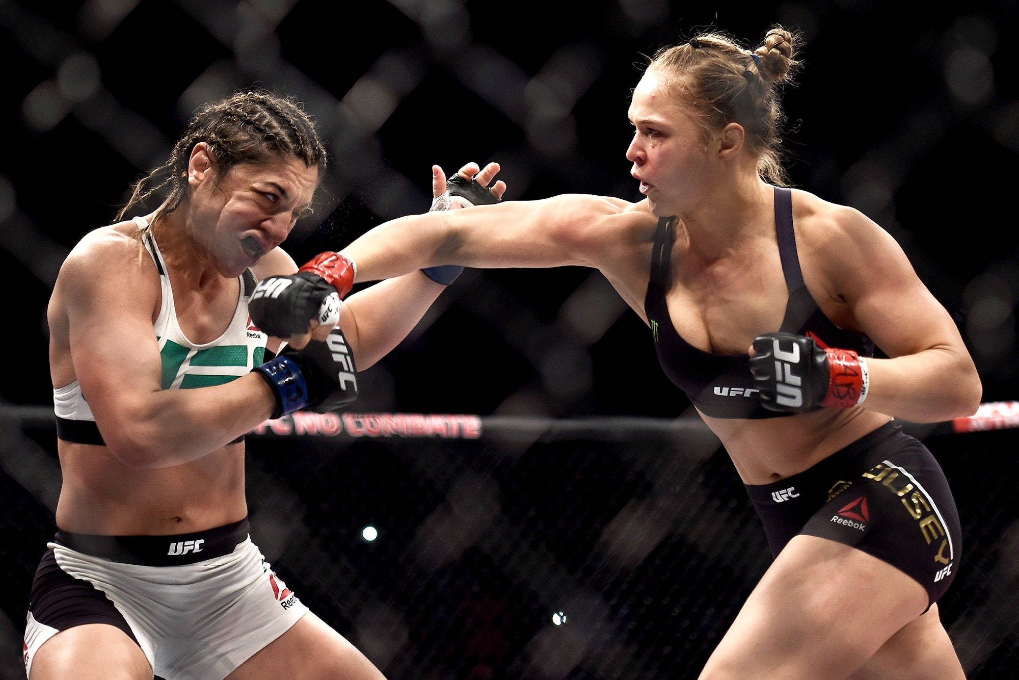 Rousey 桌布 壁紙 — 兩名女性MMA拳手在籠中激烈交鋒，一人出拳，另一人阻擋，場面高強度。