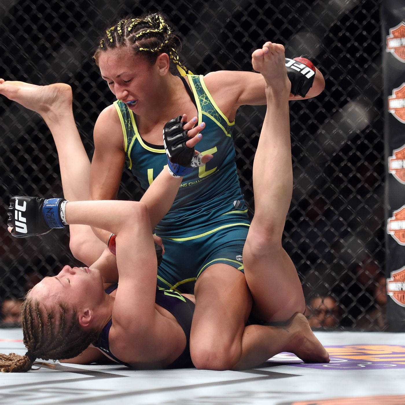 MMA 桌布 壁紙 — 兩名女性MMA拳手在籠內地板上激烈糾纏，一人施展腳鎖，另一人以強烈決心防守。