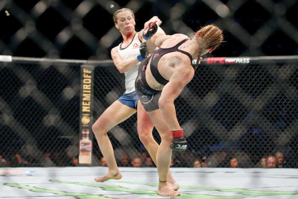 桌布 壁紙 — 兩名女拳手在UFC八角籠中交鋒，其中一人打出強力一拳，另一人則在防守。
