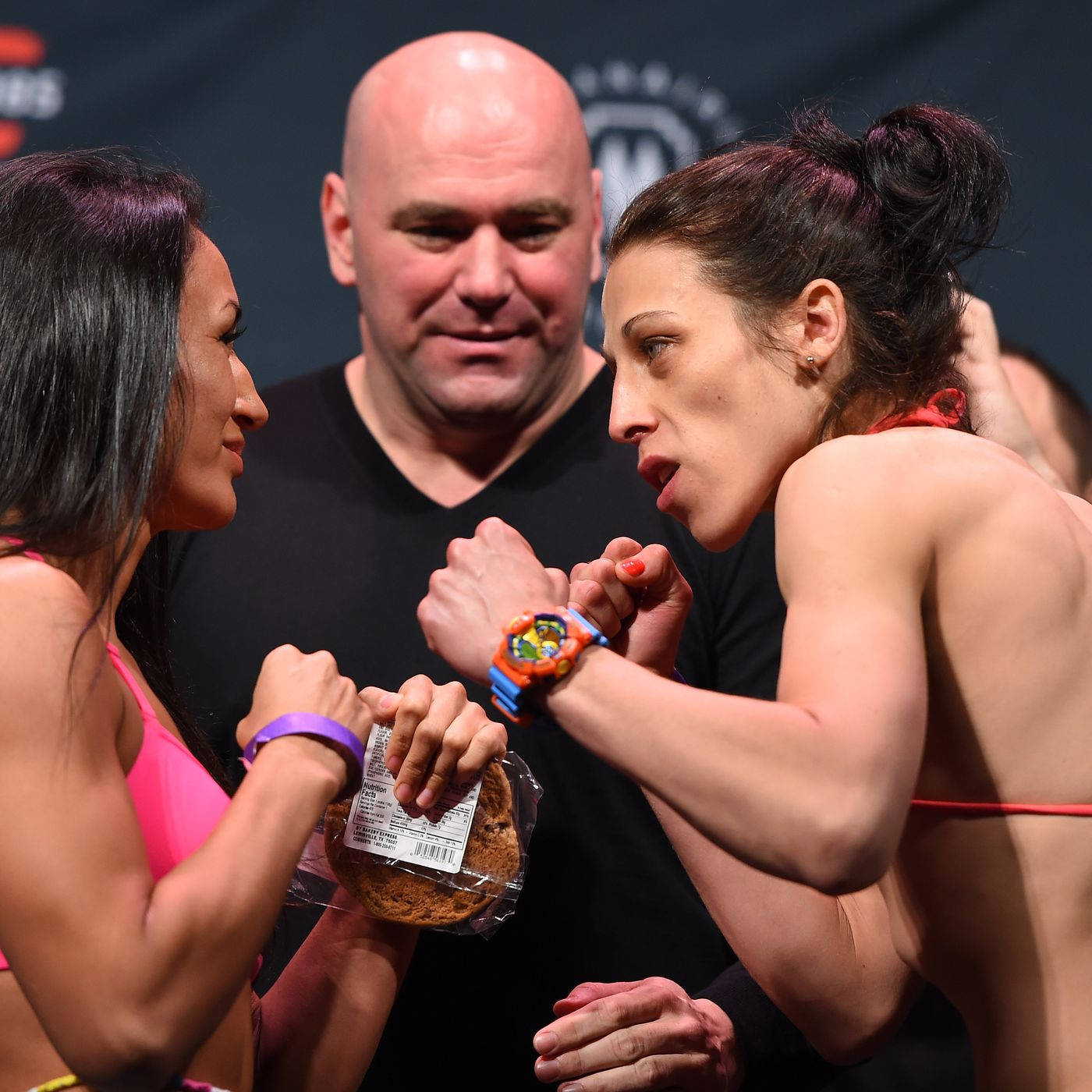 MMA 桌布 壁紙 — 兩名女拳手在賽前對峙中激烈對視，手中拿著一塊餅乾。