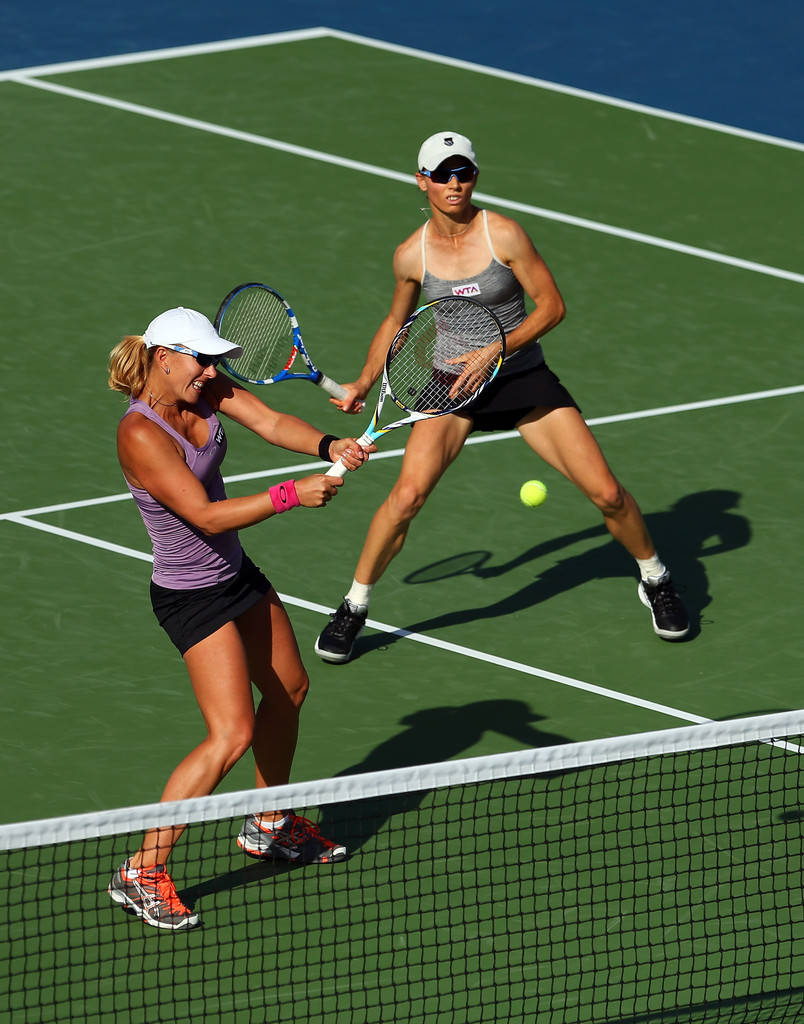 Tennis 桌布 壁紙 — 兩名女網球選手在綠色球場上激烈對打，在明亮陽光下專注擊球。