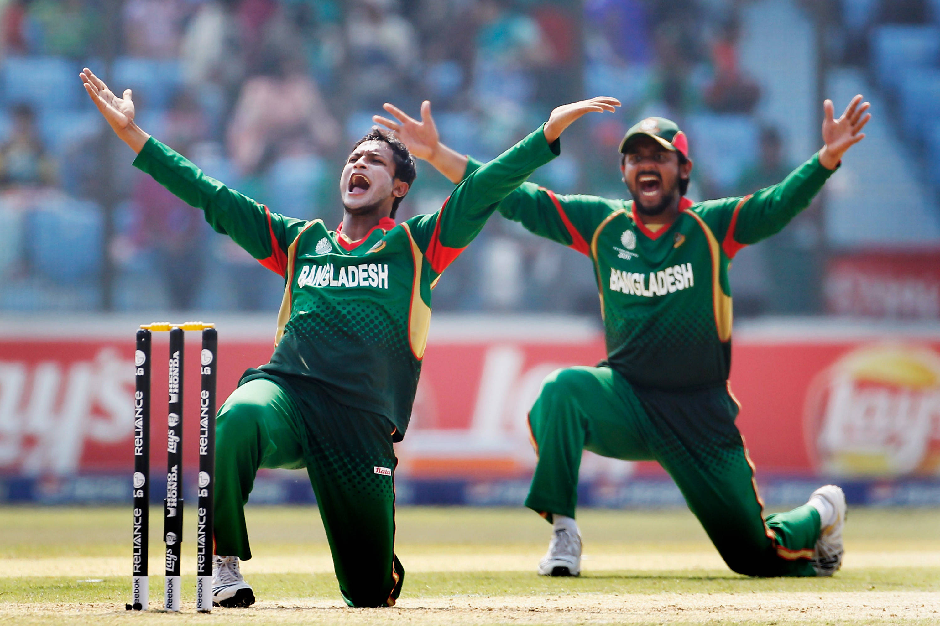 Bangladesh Cricket 桌布 壁紙 — 兩名孟加拉板球運動員在陽光明媚的球場上跪在三柱門旁，興奮地歡呼勝利。