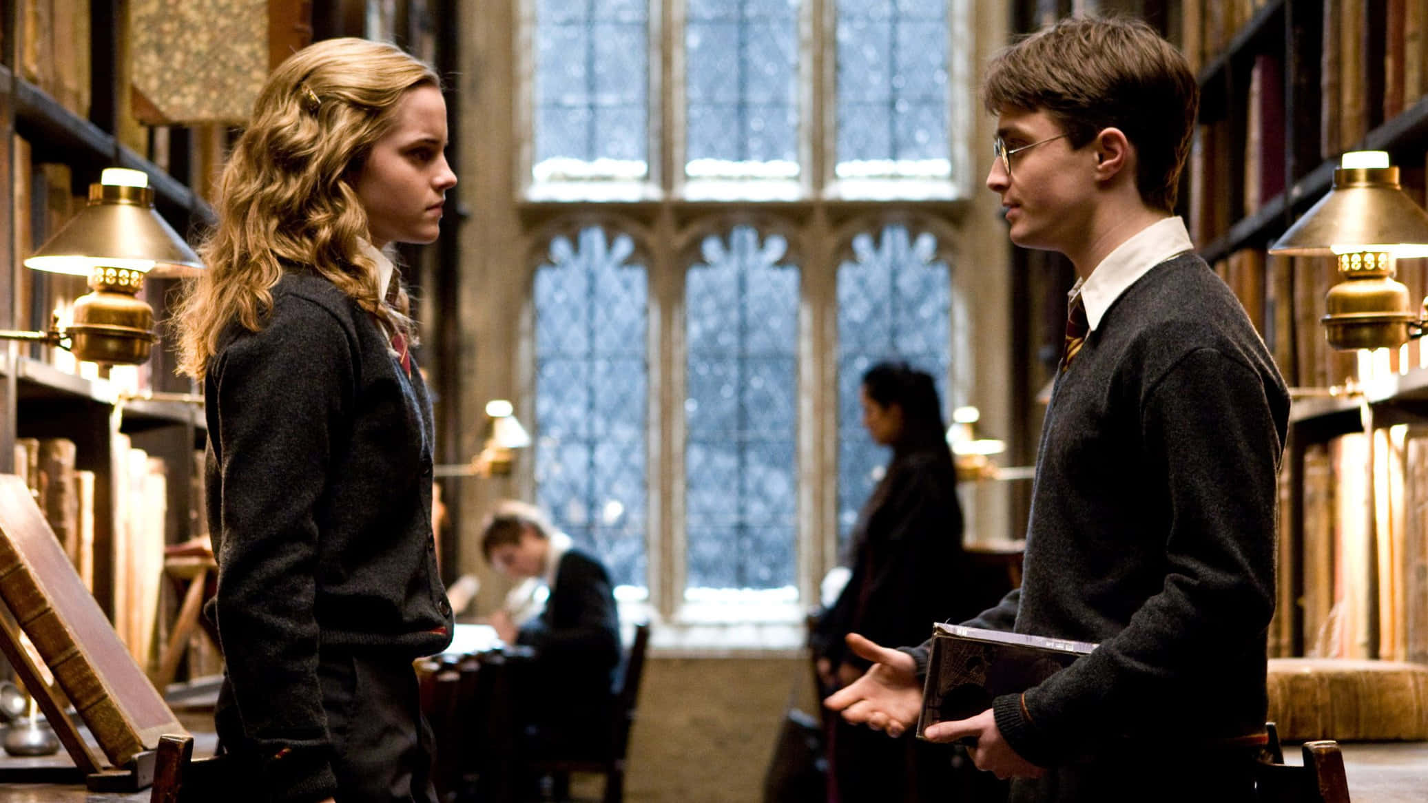Harry Potter Landscape 桌布 壁紙 — 兩名學生在一個擁有高聳書架和彩色玻璃窗、投射柔和光線的宏偉圖書館中對峙。