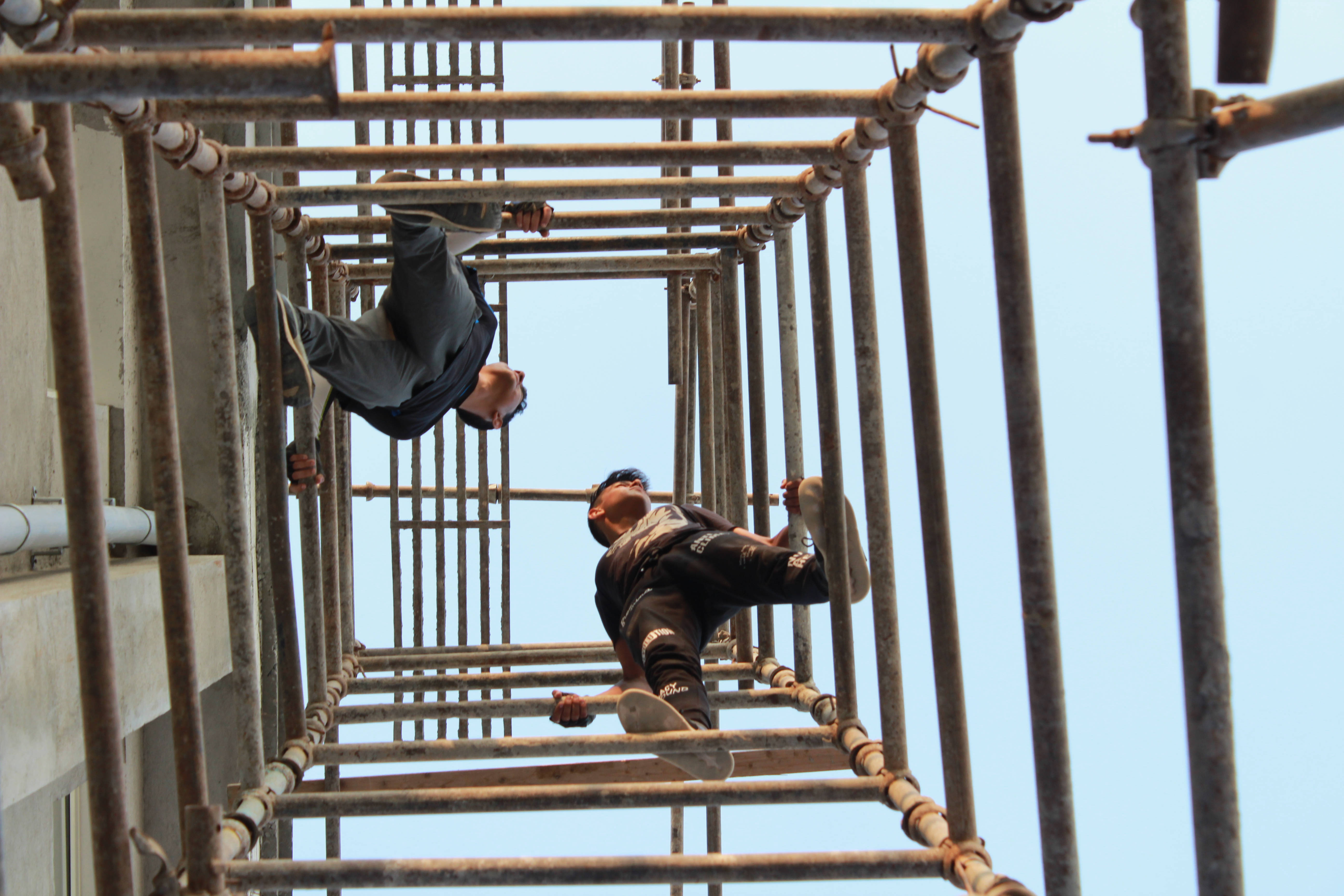 Parkour 桌布 壁紙 — 兩名工人倒掛在金屬鷹架上，背景是晴朗的藍天，正在進行日間施工。