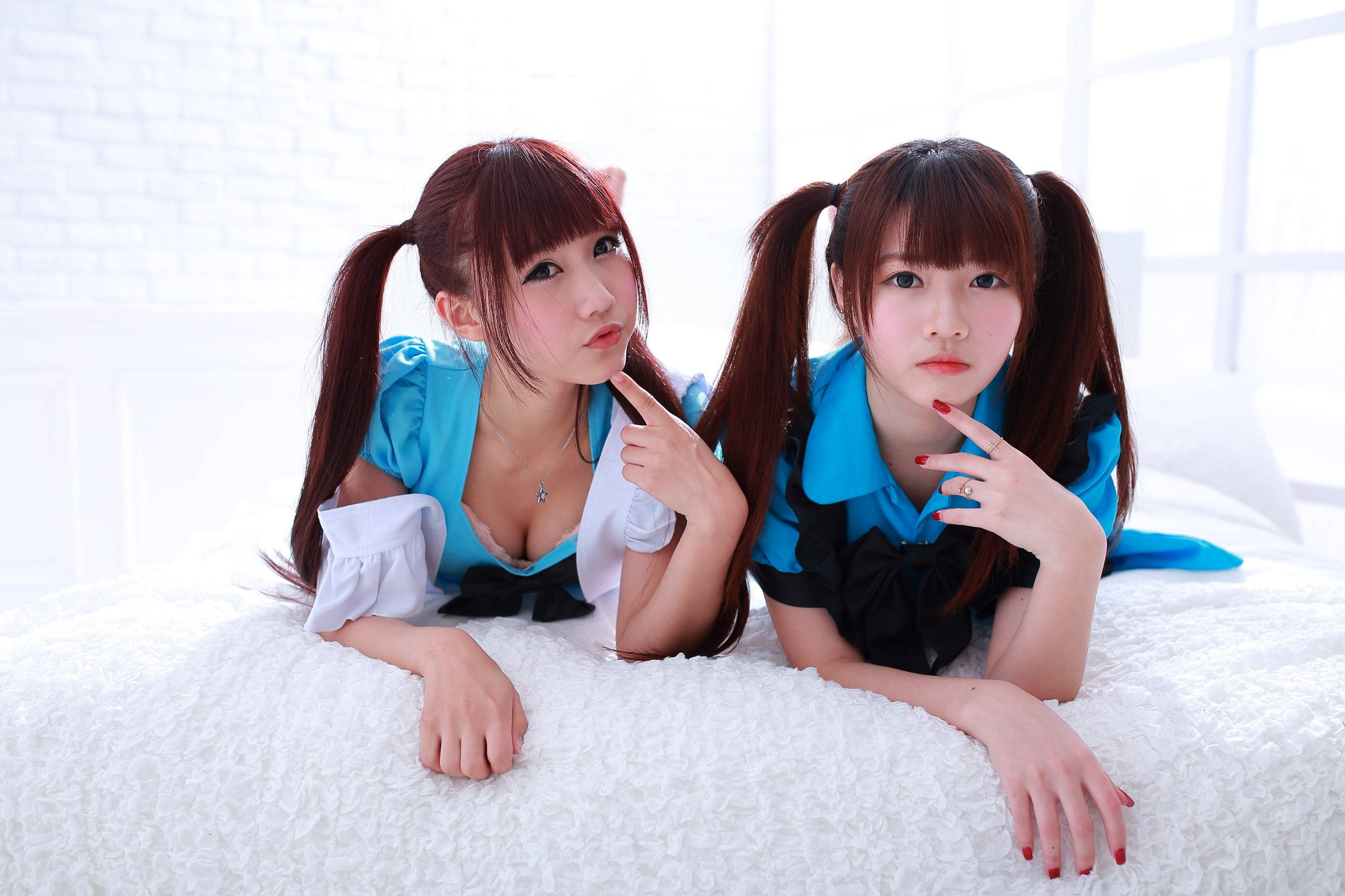 cosplay 桌布 壁紙 — 兩名年輕女性身穿藍色女僕裝，紮著辮子，在 fluffy 白色床上對著明亮的白色磚牆俏皮地擺姿勢。