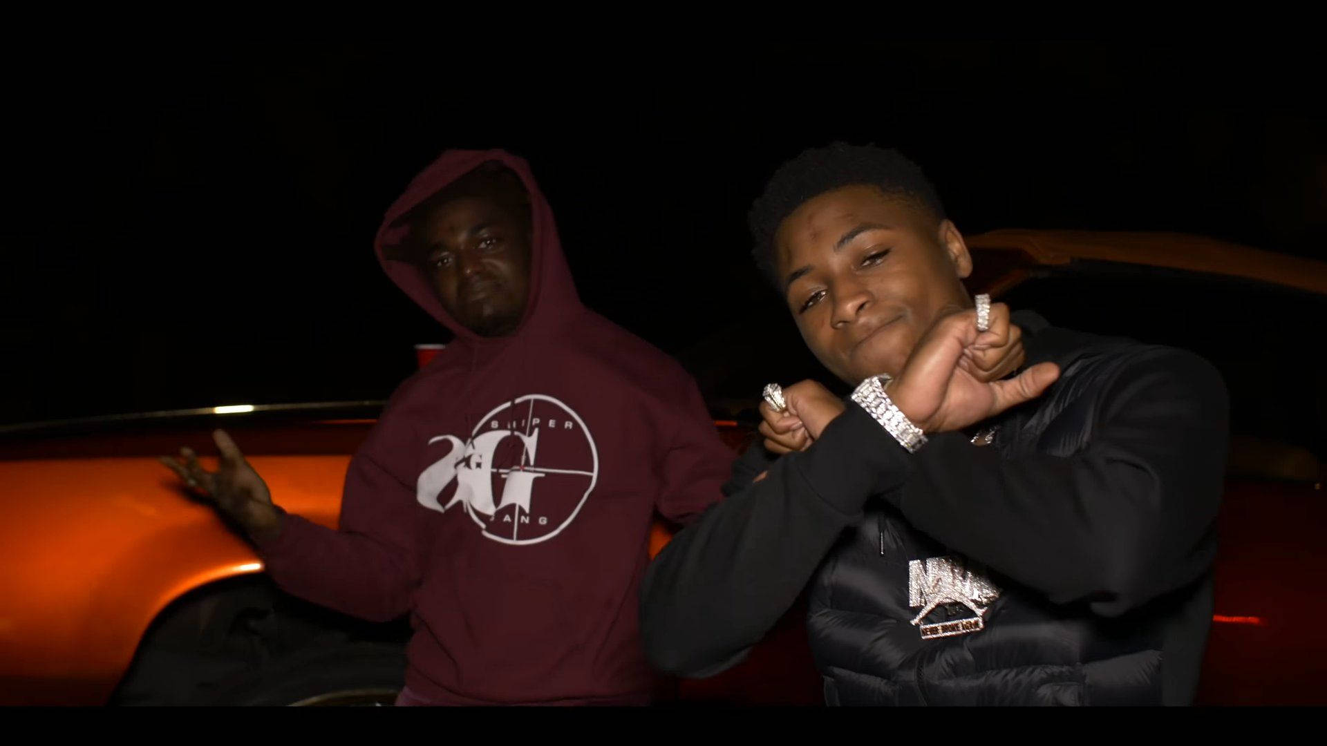 Youngboy 桌布 壁紙 — 兩名年輕男子在夜間自信地站在一輛發光的橙色跑車旁，佩戴著閃亮的珠寶和品牌連帽衫。
