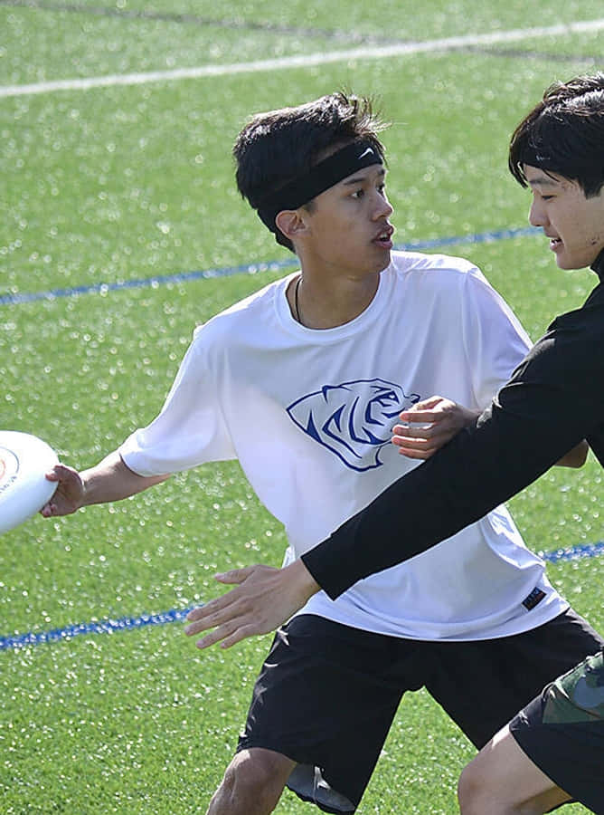 Athlete 桌布 壁紙 — 兩名年輕男子在明亮的綠色草地上激烈競爭，其中一人準備擲出白色飛盤。