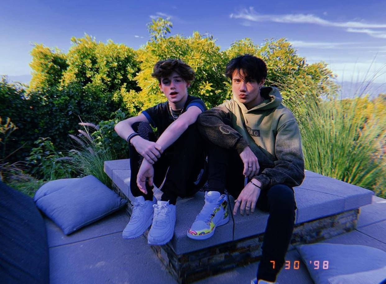 Payton 桌布 壁紙 — 兩名年輕男子在晴朗藍天下，隨意坐在被茂密綠植環繞的石凳上。