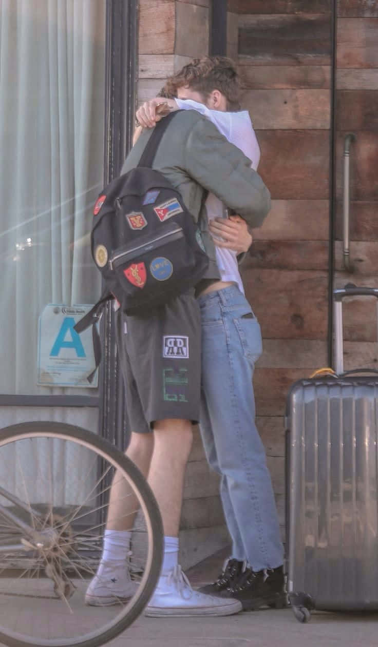 Hugging 桌布 壁紙 — 兩名年輕男子在木建築外熱情擁抱，附近有一輛腳踏車和一個行李箱。