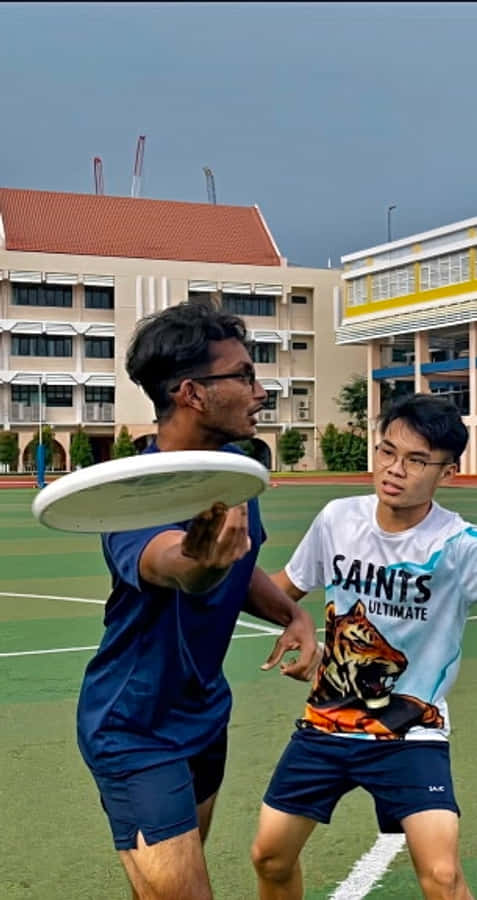 Android Ultimate Frisbee 桌布 壁紙 — 兩名年輕男子在綠色運動場上激烈競爭，其中一人將白色飛盤擲向另一人。