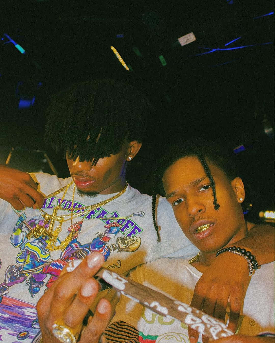 Rappers 桌布 壁紙 — 兩名年輕男子戴著金牙和鏈條，在燈光昏暗、霓虹燈閃爍的俱樂部中擺出強烈的姿勢。