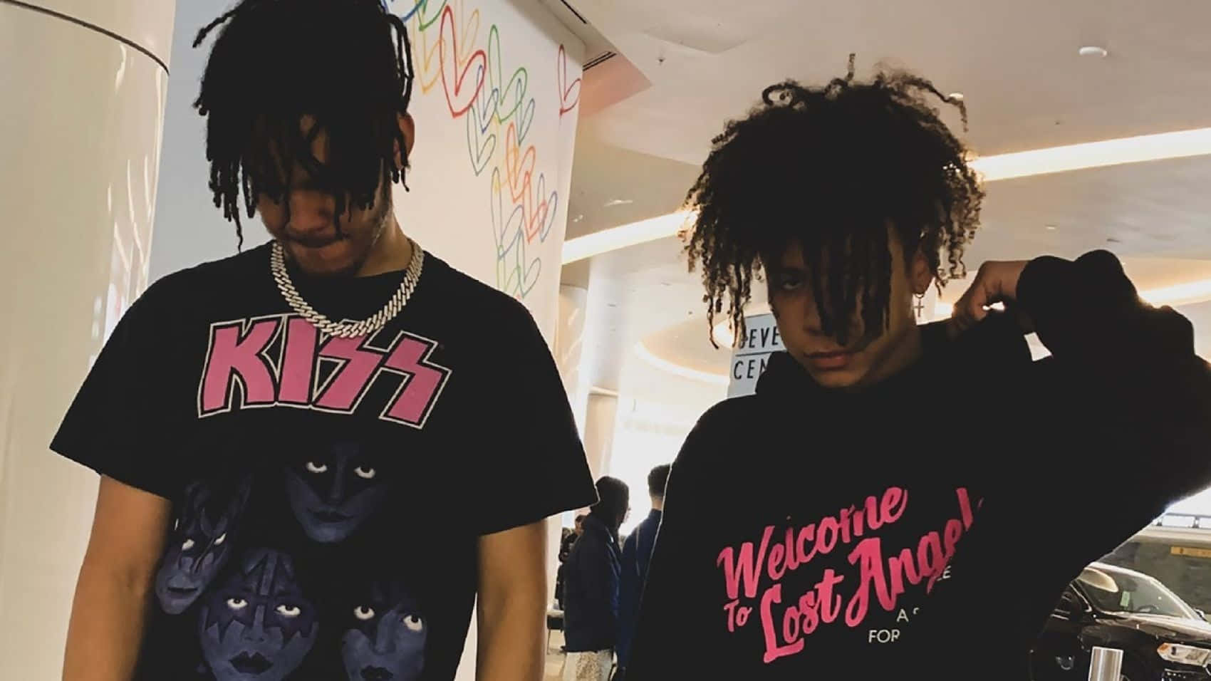Hip Hop 桌布 壁紙 — 兩名年輕男子留著辮子頭在室內擺姿勢，一人穿著Kiss T恤，另一人穿著Welcome to Lost Angeles連帽衫。