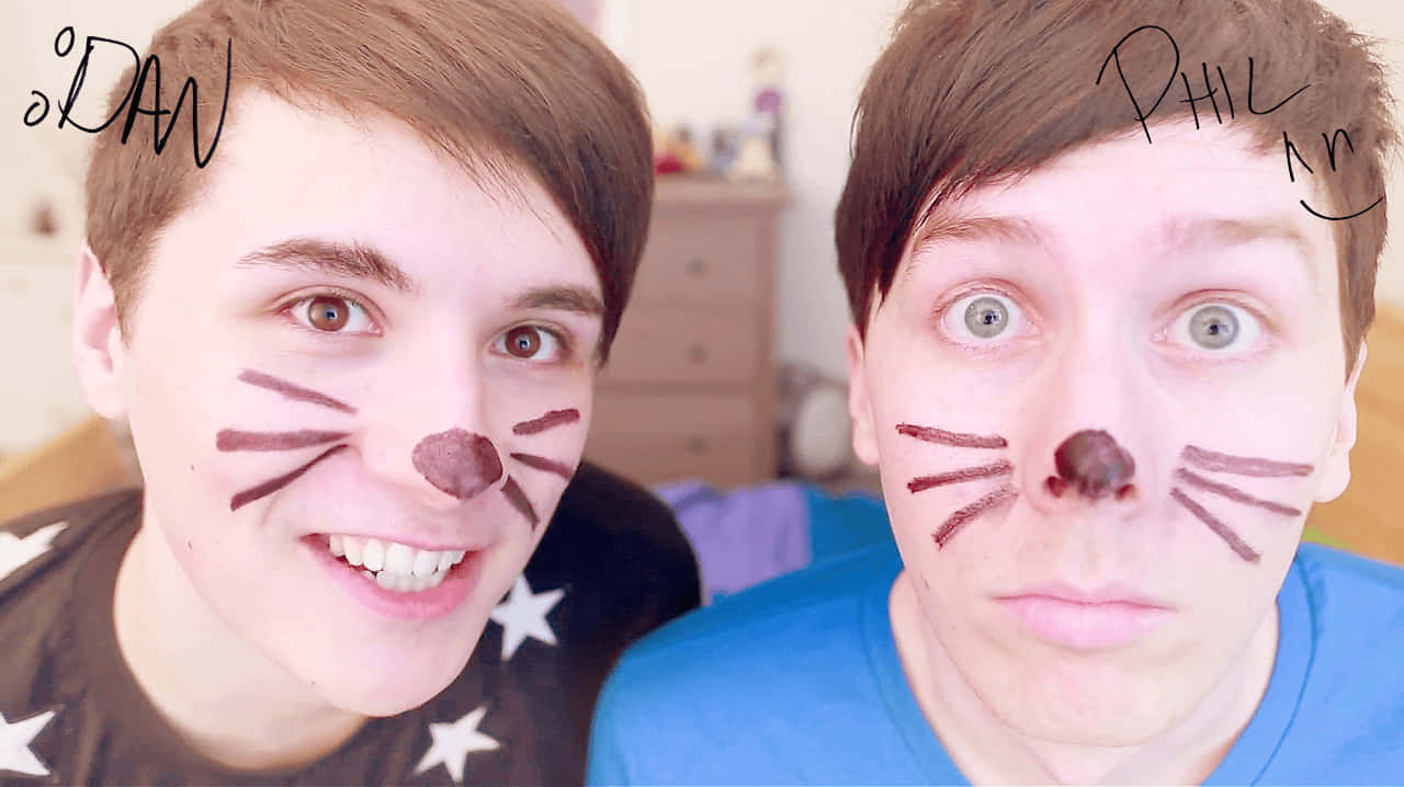 dan and phil 桌布 壁紙 — 兩名年輕男子臉上畫著貓咪妝，在舒適的臥室環境中微笑並凝視鏡頭。