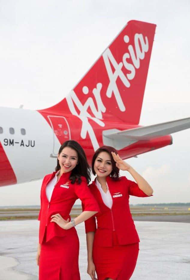 Aircraft 桌布 壁紙 — 兩名微笑的亞洲航空空服員身穿紅色制服，在停機坪上一架紅白相間的飛機前自信地擺姿勢。