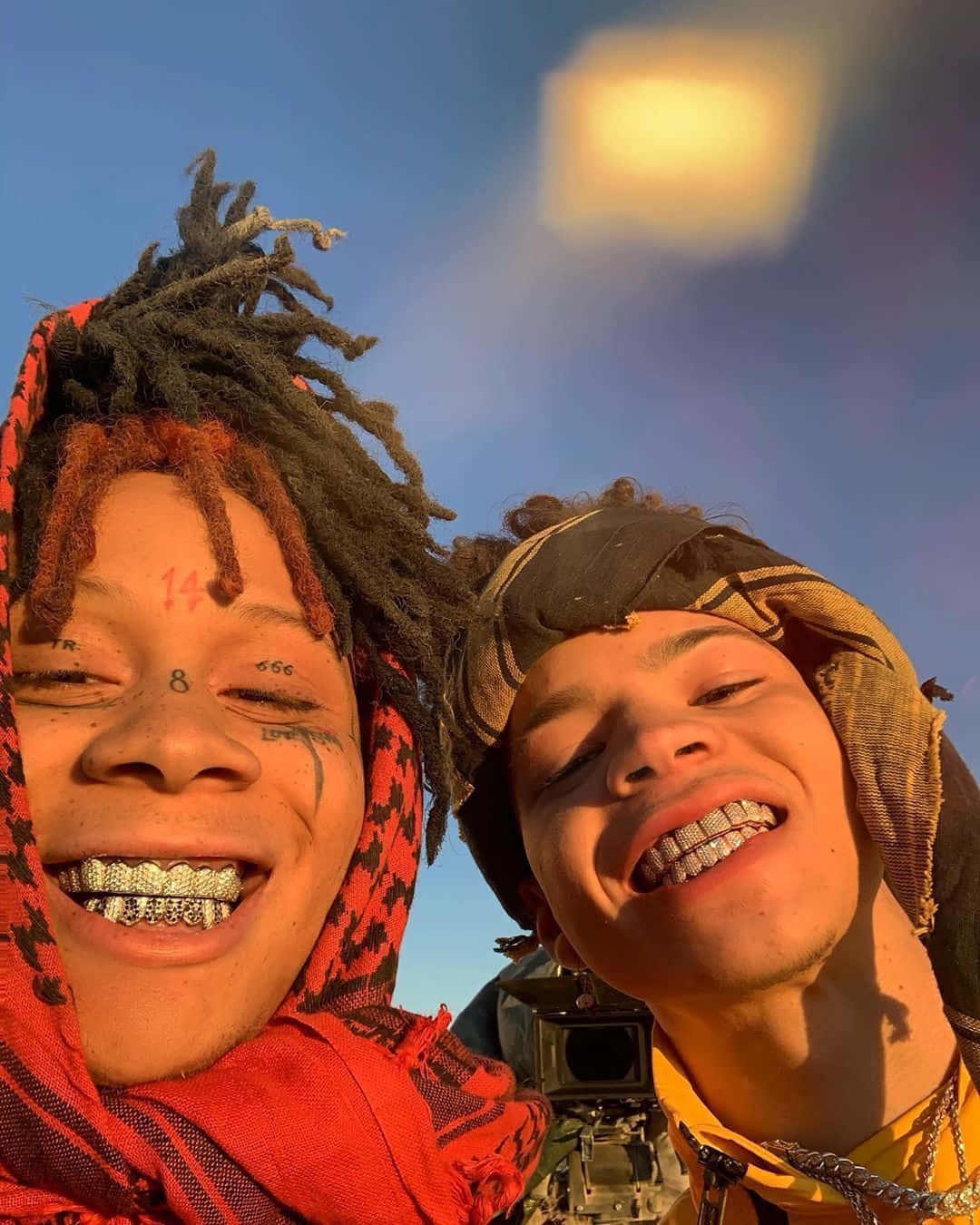 Lil Mosey 桌布 壁紙 — 兩名微笑的年輕男子，編著辮子頭髮，戴著鑽石牙套，在溫暖的日落天空下擺姿勢。