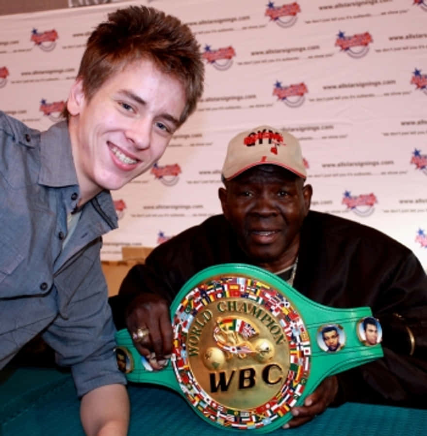 Champion 桌布 壁紙 — 兩名微笑的男子在品牌背景前，手持綠色WBC拳擊冠軍腰帶擺姿勢。