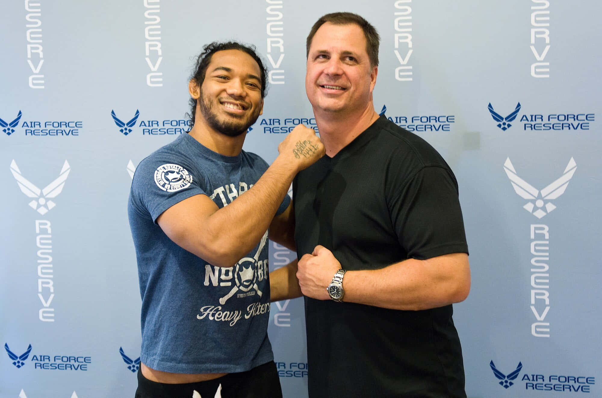 MMA 桌布 壁紙 — 兩名微笑的男子穿著T恤，在藍色空軍預備役品牌背景前拍照。