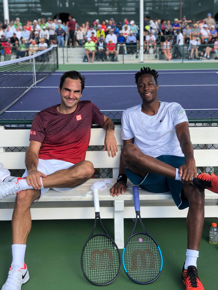 Tennis 桌布 壁紙 — 兩名微笑的網球運動員坐在藍色球場的白色長椅上，球拍放在旁邊，觀眾從後面的看台觀看。