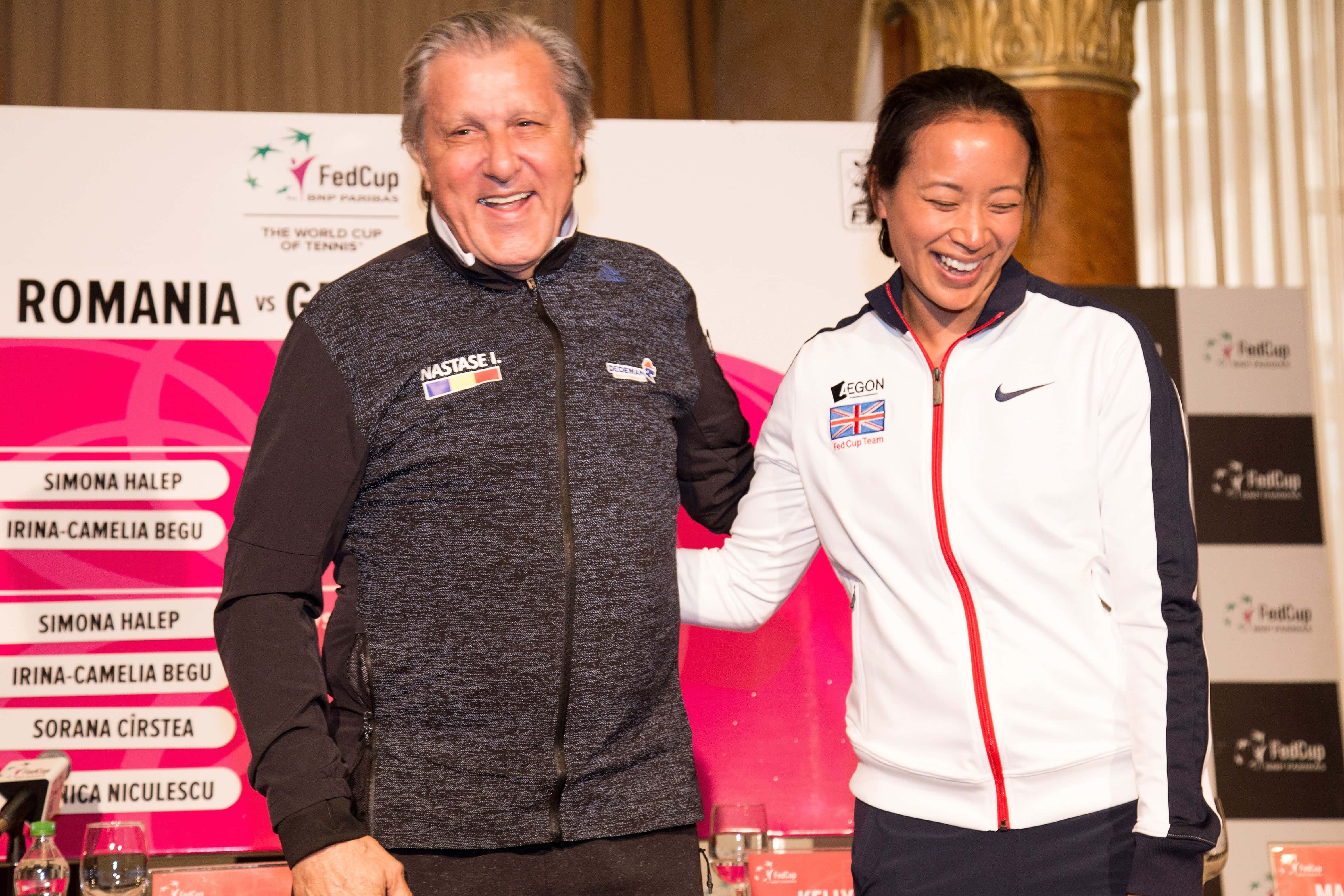 Tennis 桌布 壁紙 — 兩名微笑的網球選手穿著隊服外套，在有品牌背景的Fed Cup賽事中一起擺姿勢。