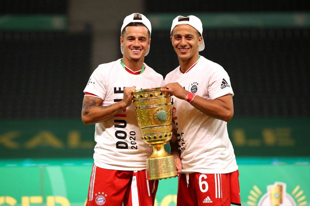 Coutinho 桌布 壁紙 — 兩名微笑的足球運動員身穿白色球衣和紅色短褲，在綠色球場上自豪地共同舉起金色獎盃。